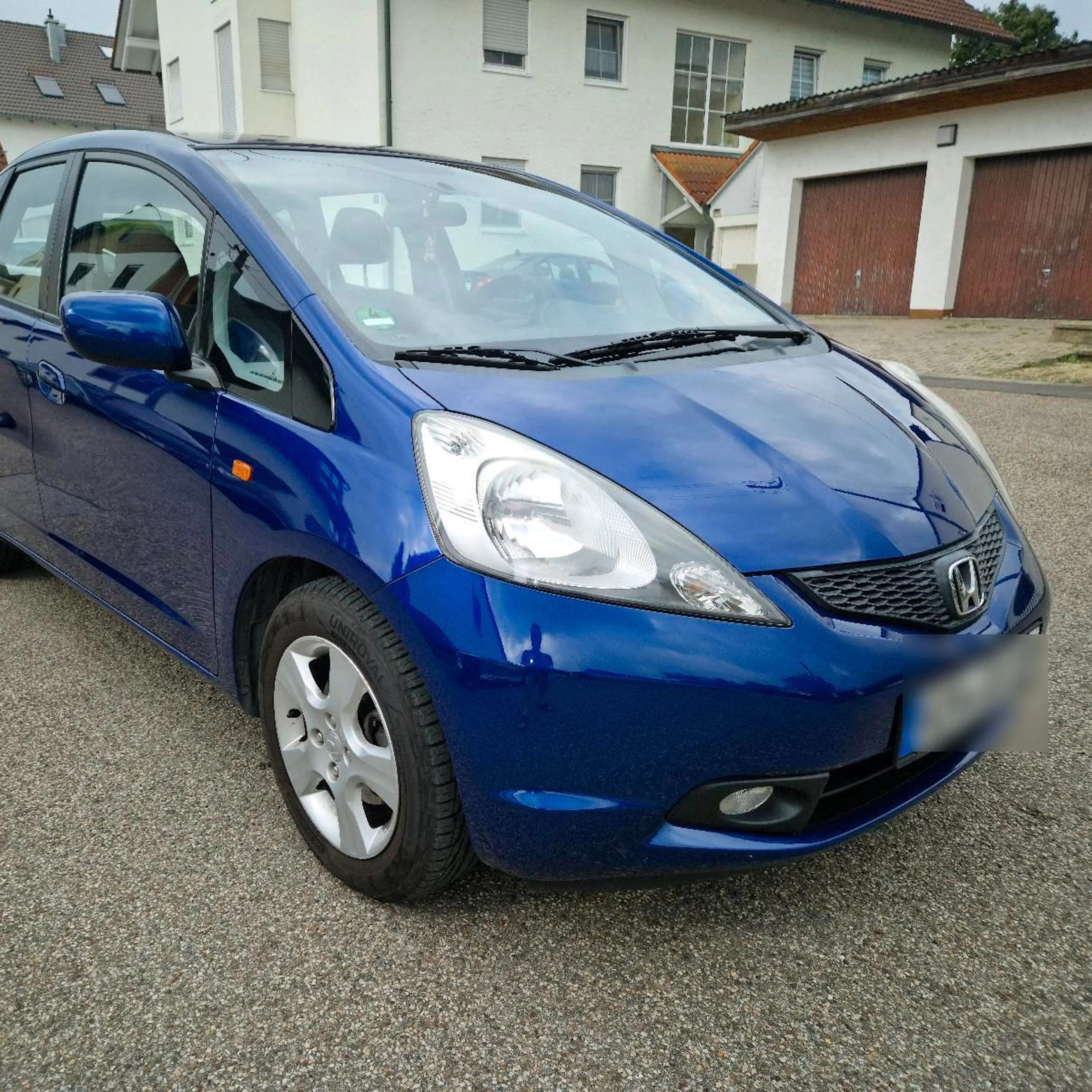 A used Honda Jazz in blue is parked in the courtyard.