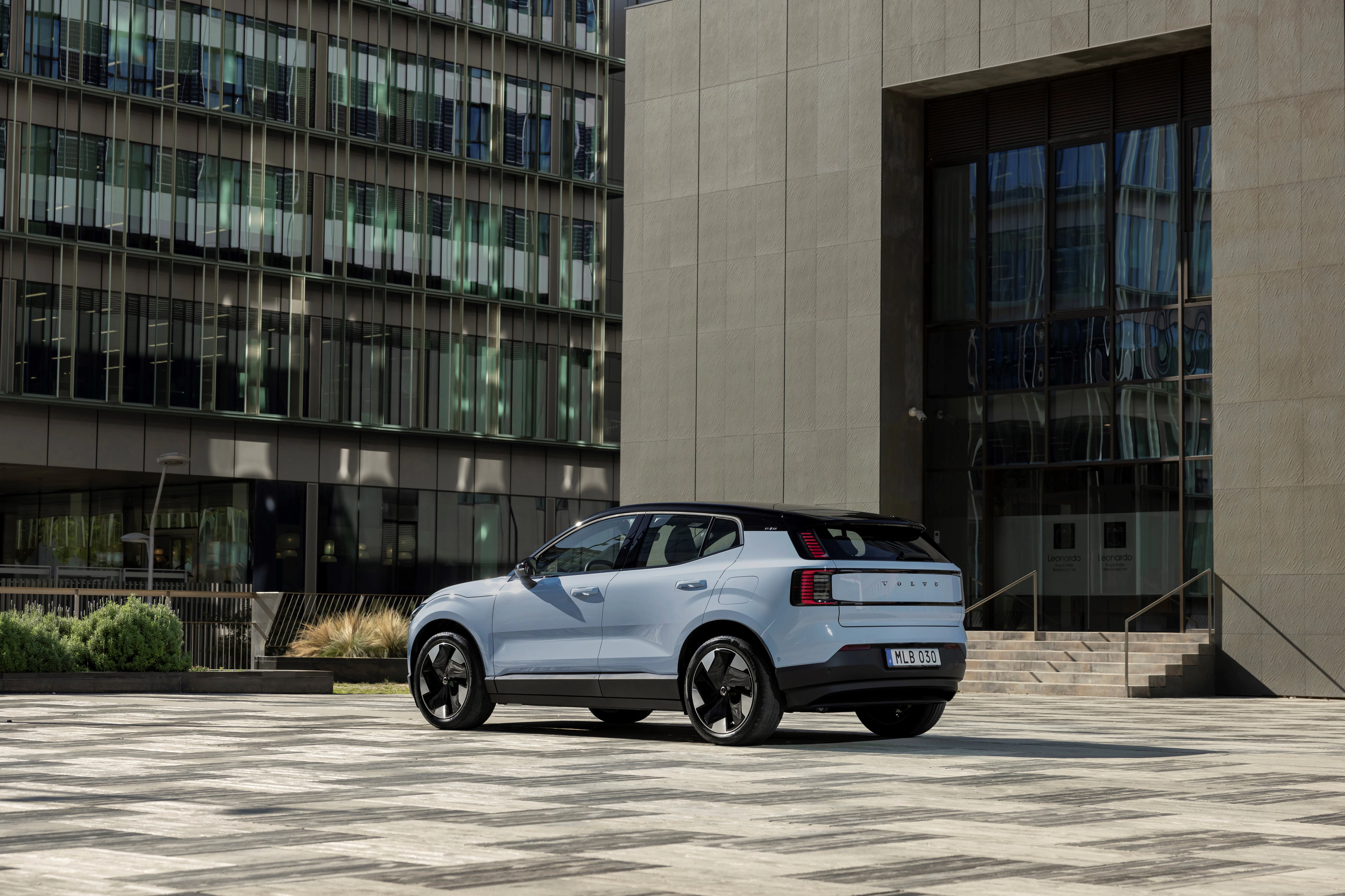Ein blauer EX30 parkt in der schrägen Heckansicht vor einem urbanen Gebäude