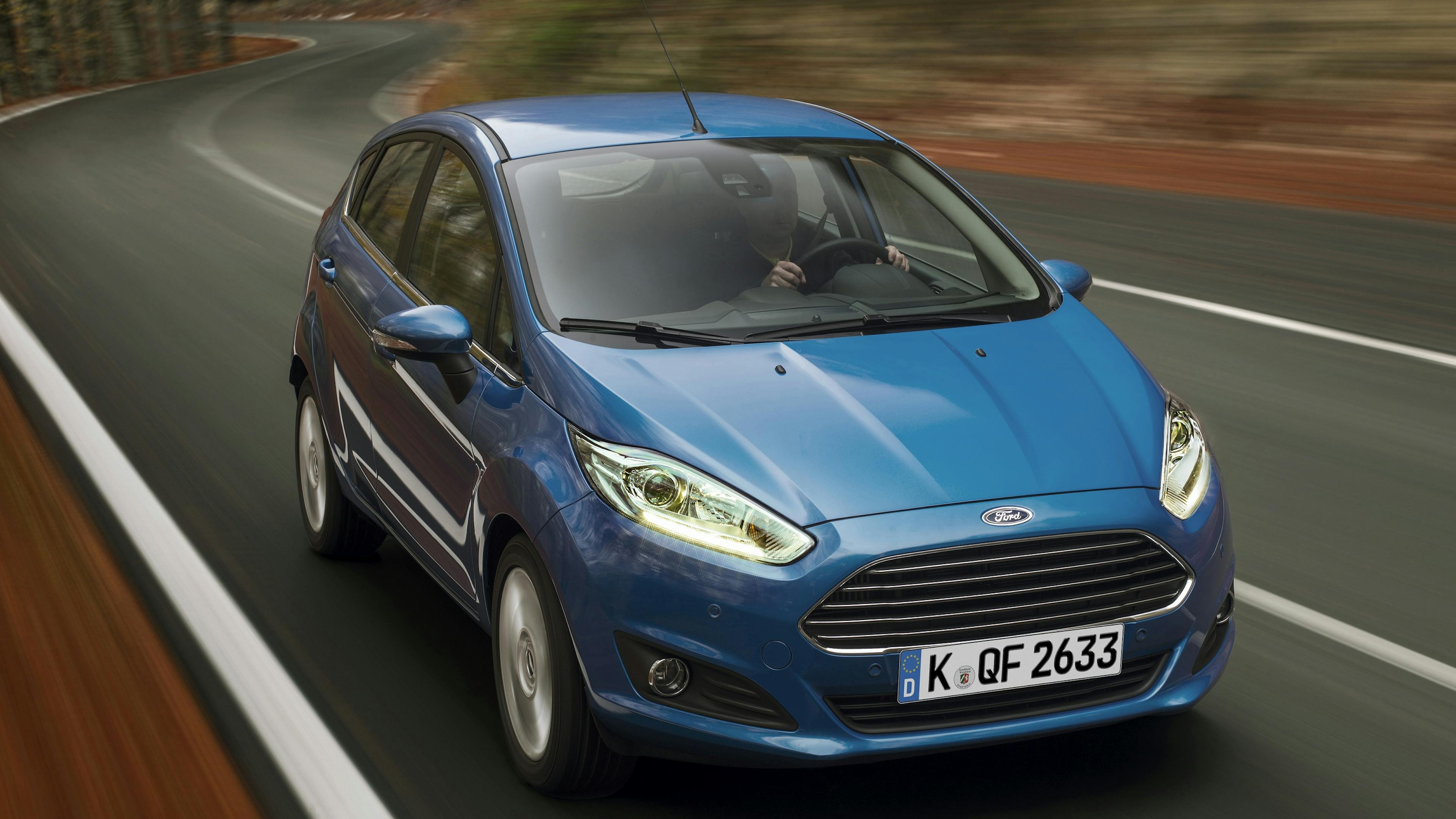 A blue Ford Fiesta four-door, photographed from the front while driving in the forest.