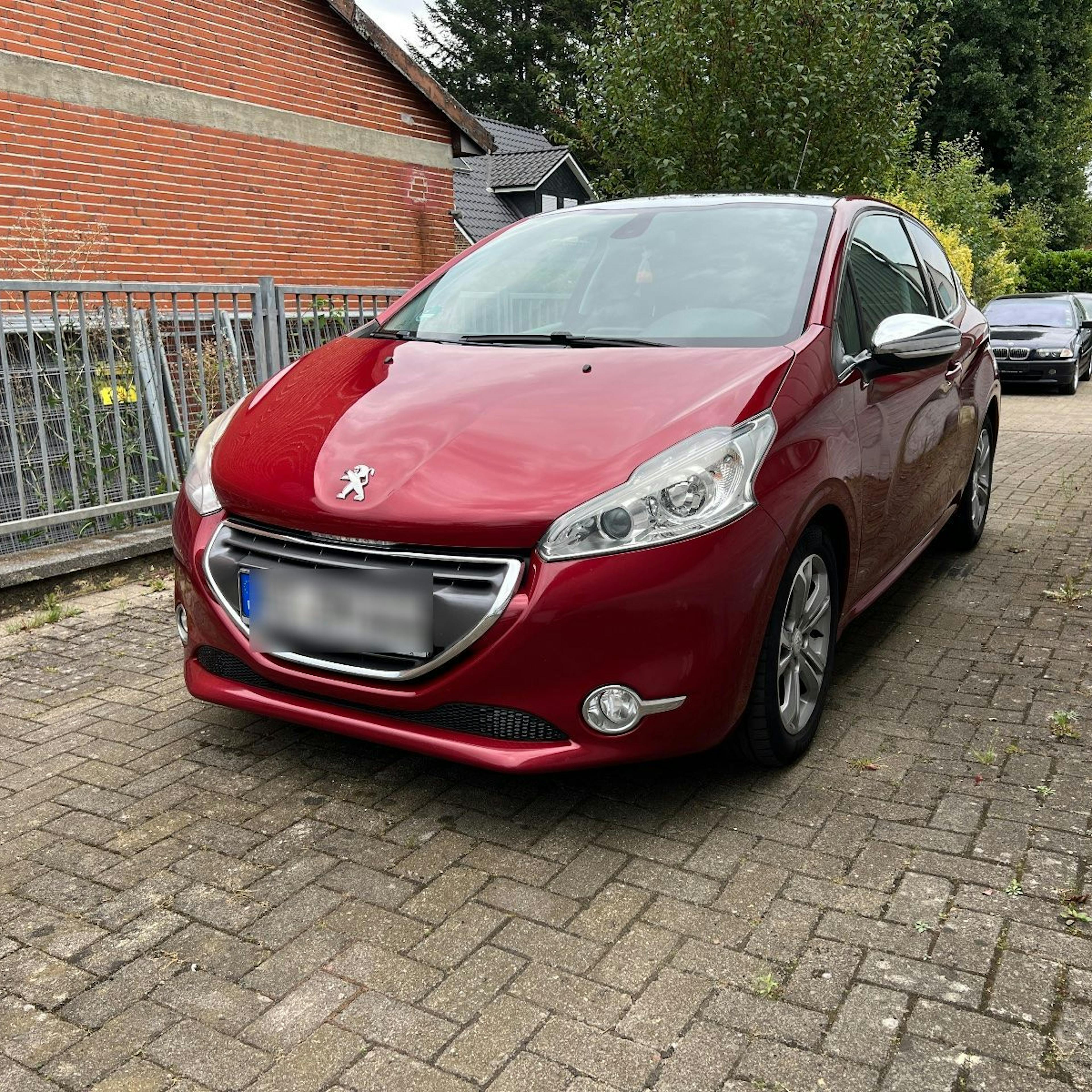 A red Peugeot 208 in a driveway