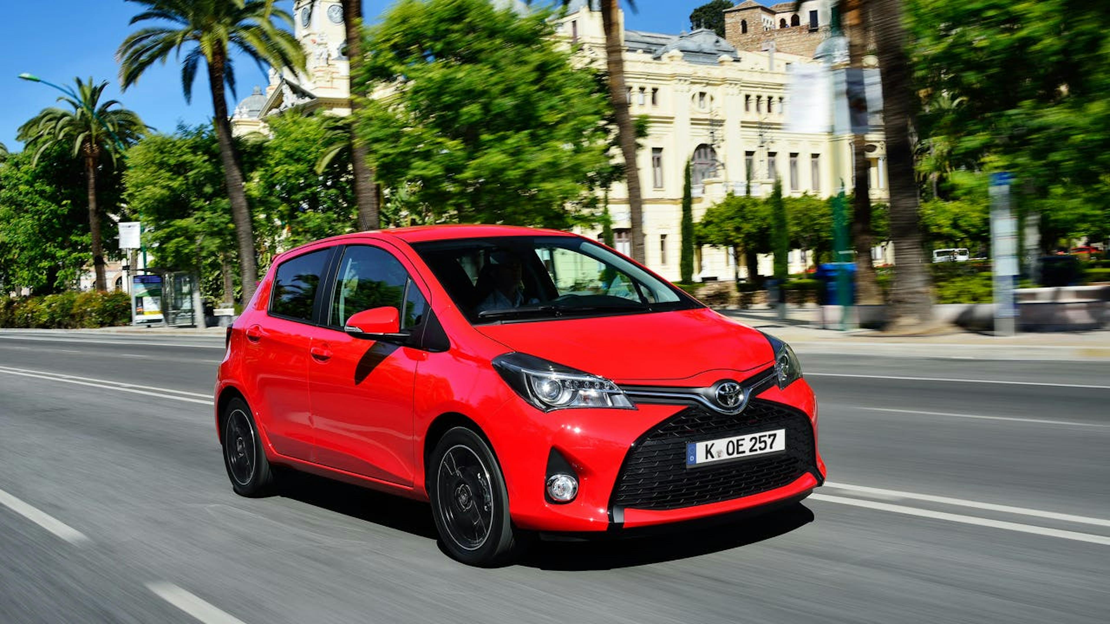 Ein roter Toyota Yaris, während der Fahrt von schräg vorne in einer südländischen Stadt fotografiert.