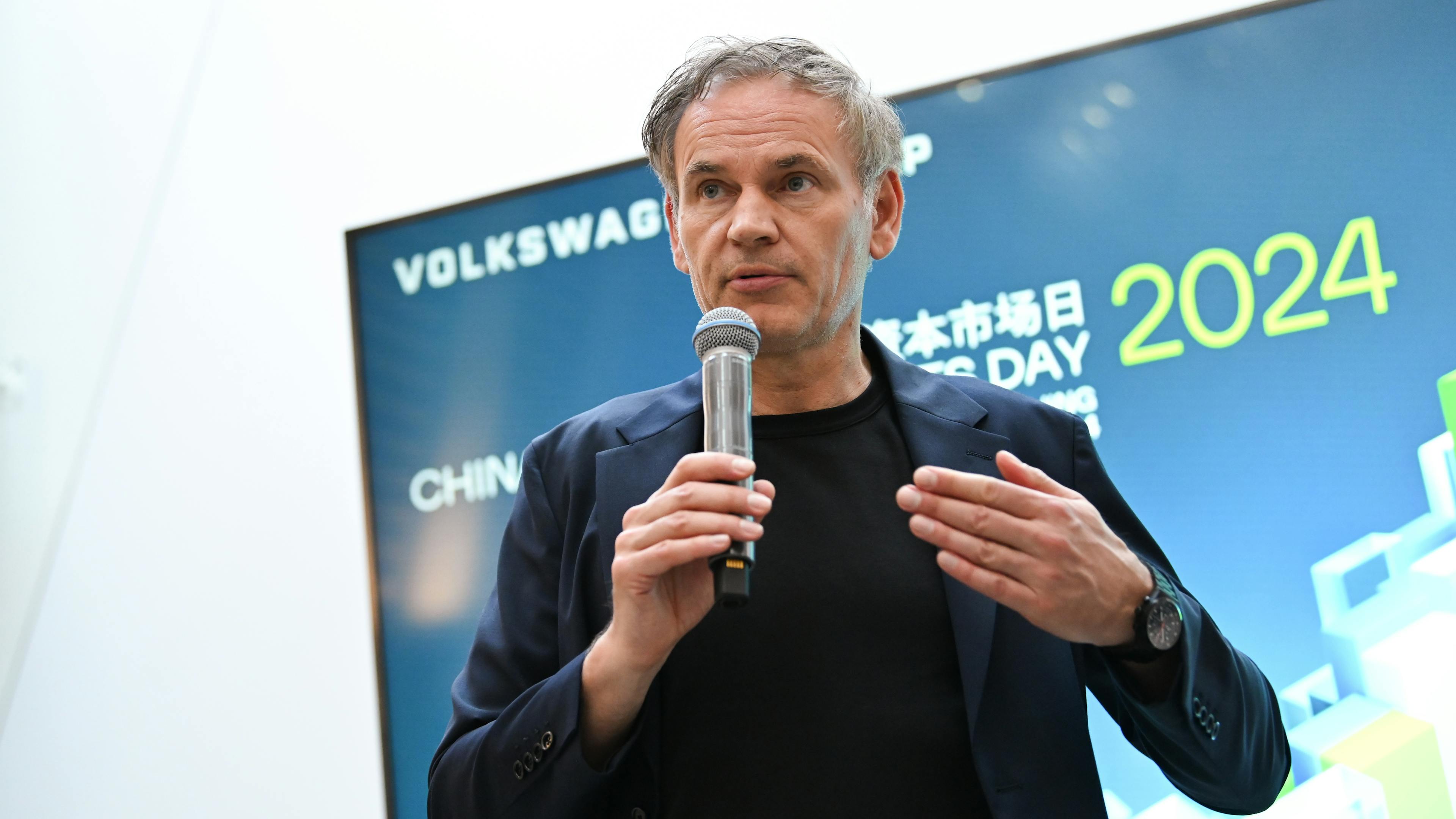 VW CEO Oliver Blume speaks into a microphone on a stage.