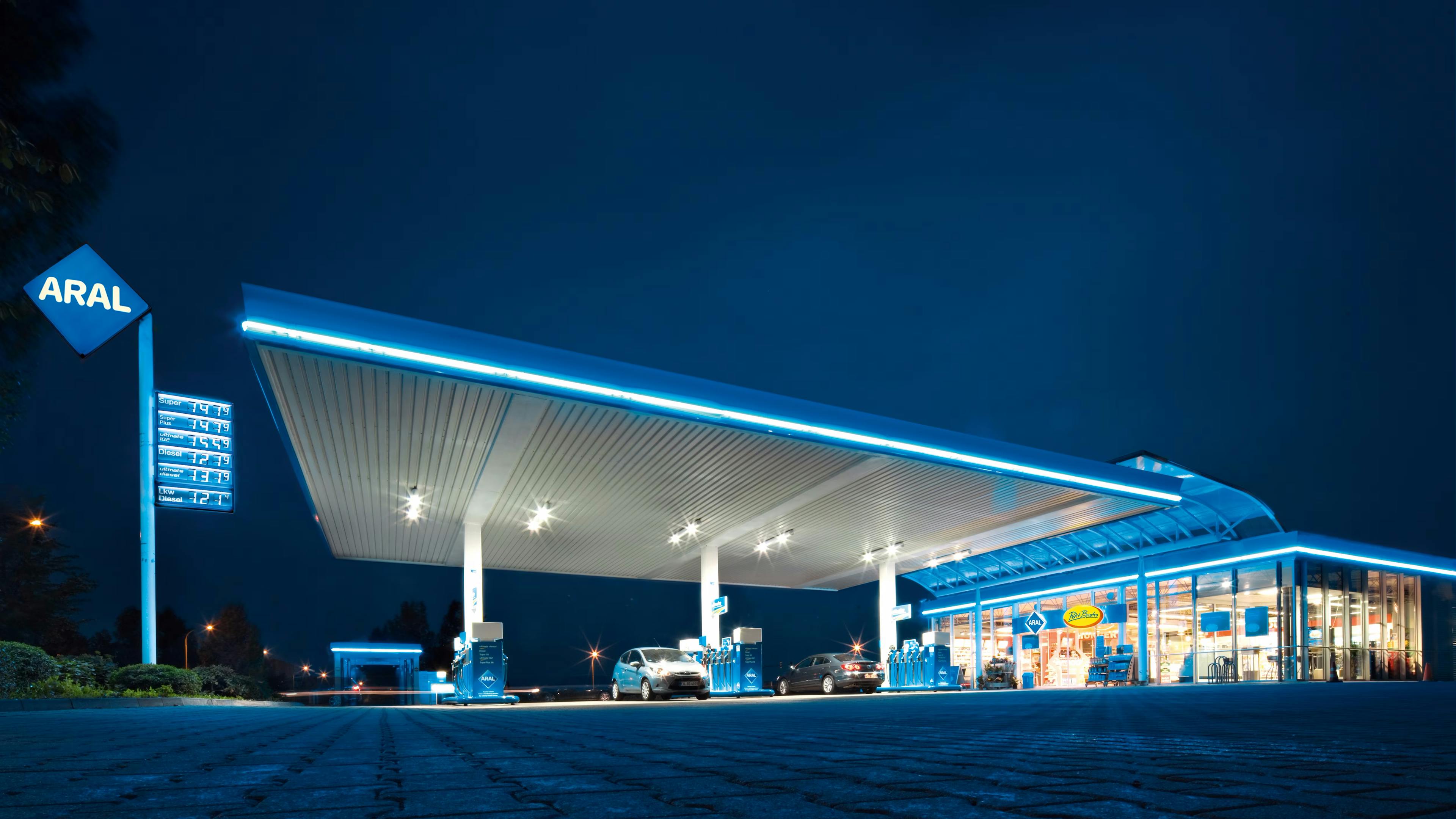 Several cars refuel in the dark at an illuminated gas station.
