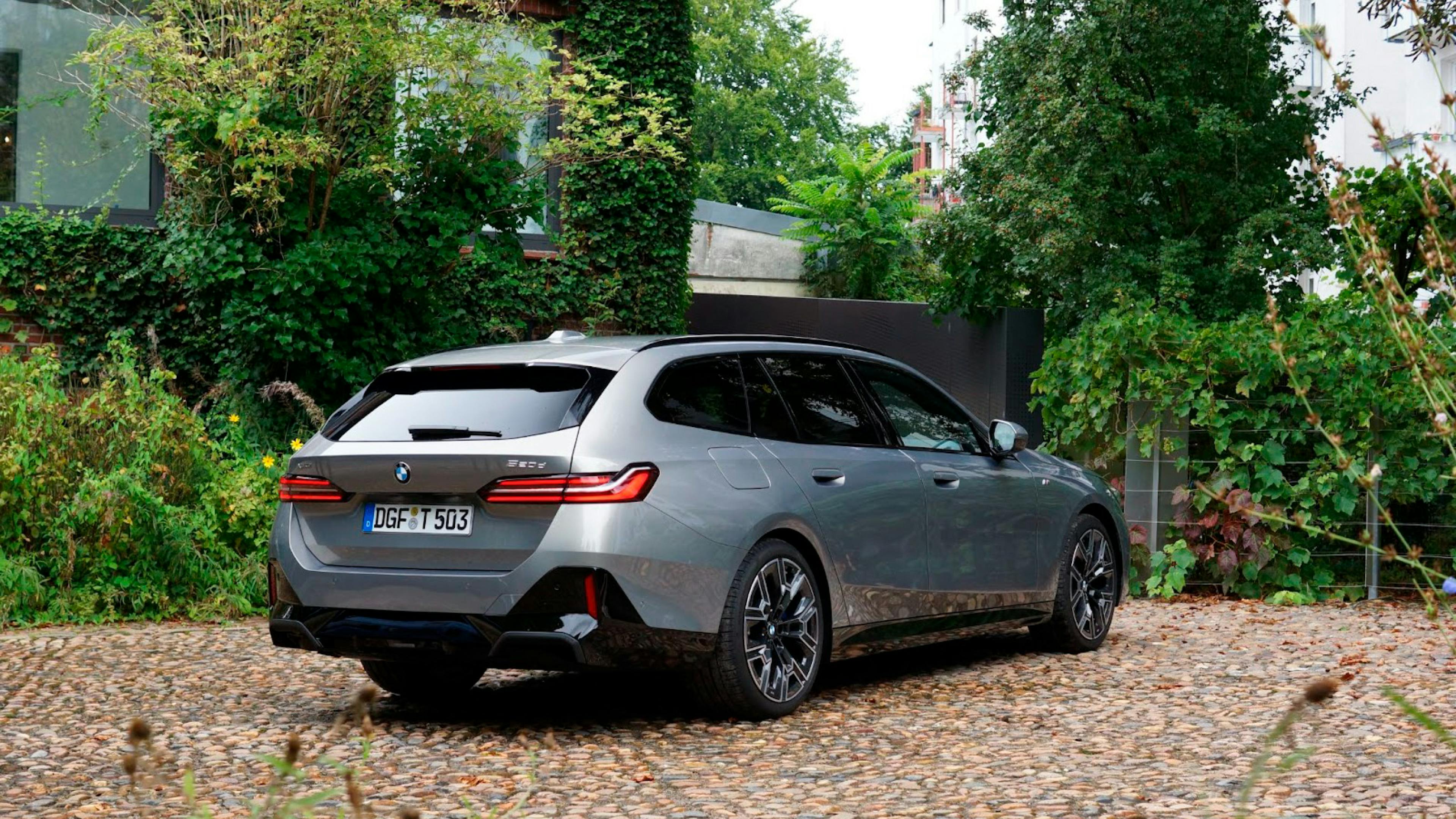 Silver BMW 5 Series Touring on a cobblestone square with a brick building in the background.