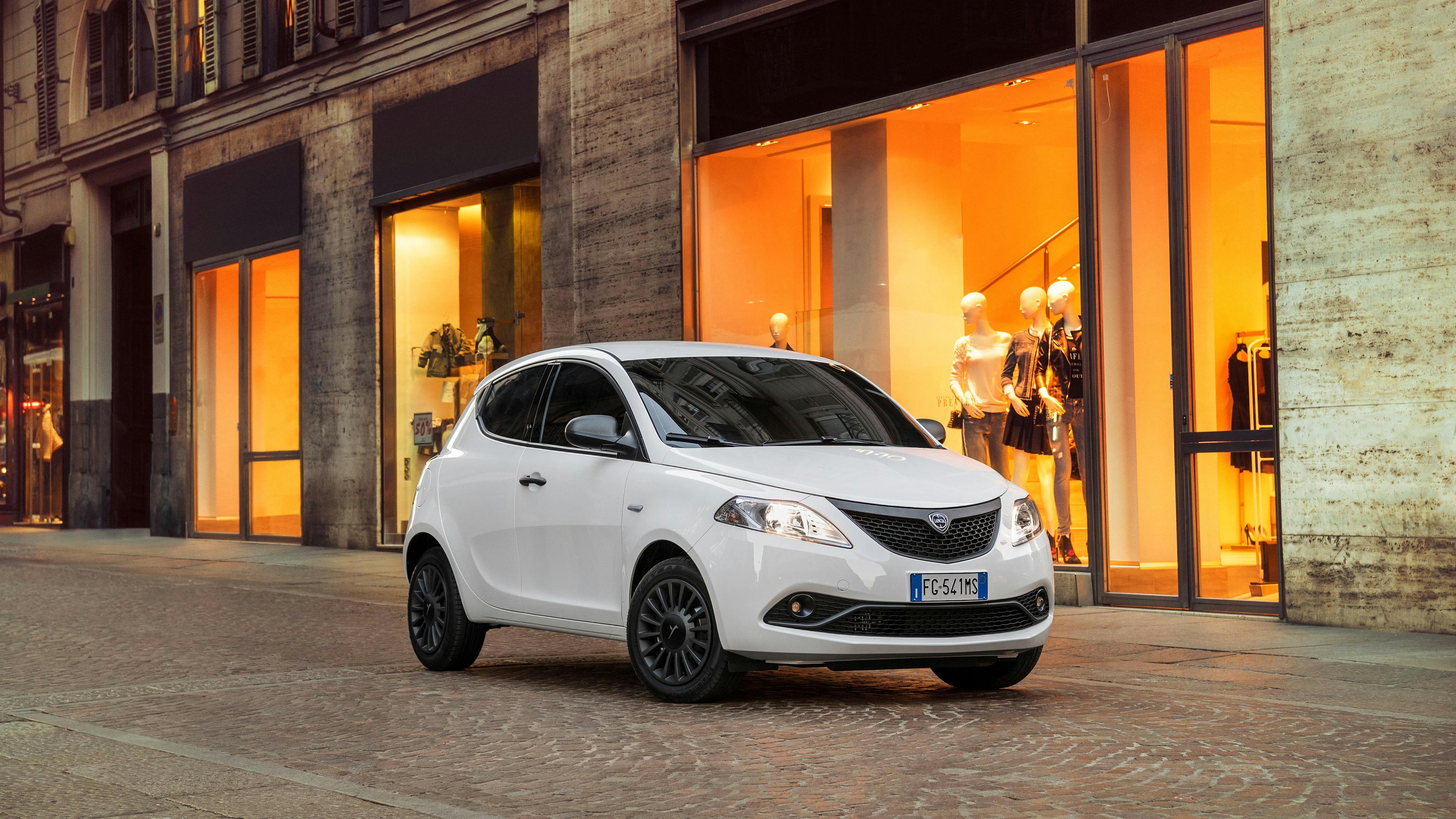 A white Lancia Ypsilon is parked in front of a boutique.