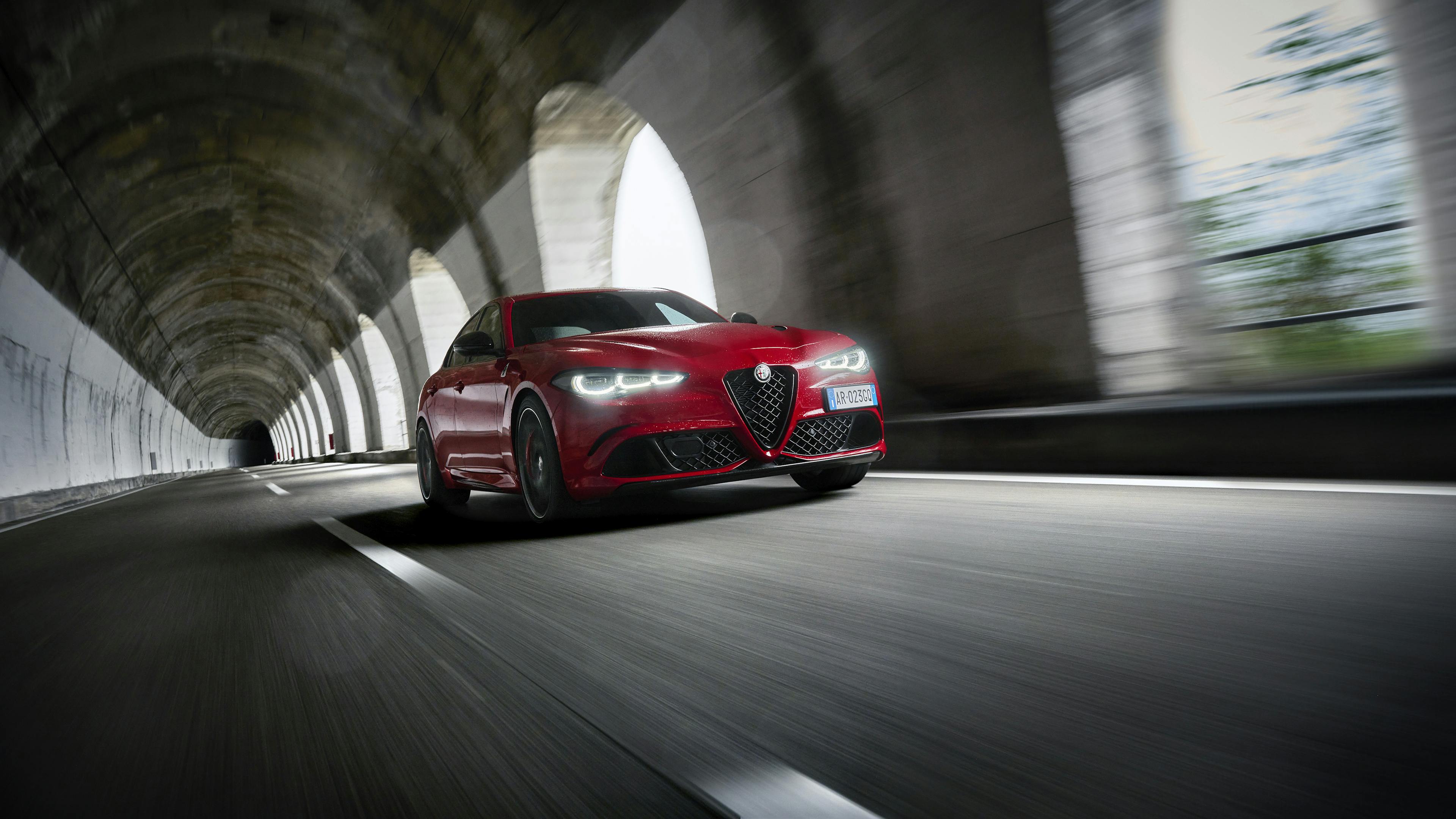 A red Alfa Romeo Giulia drives through a tunnel-like gallery.