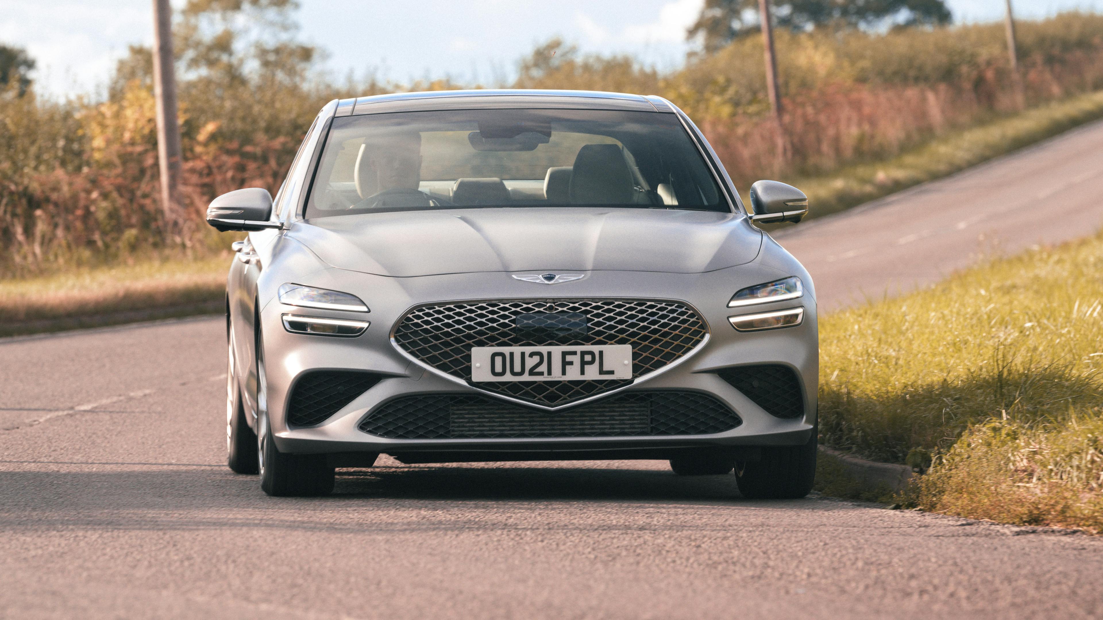 A silver-gray Genesis G70 drives through a curve on the country road.