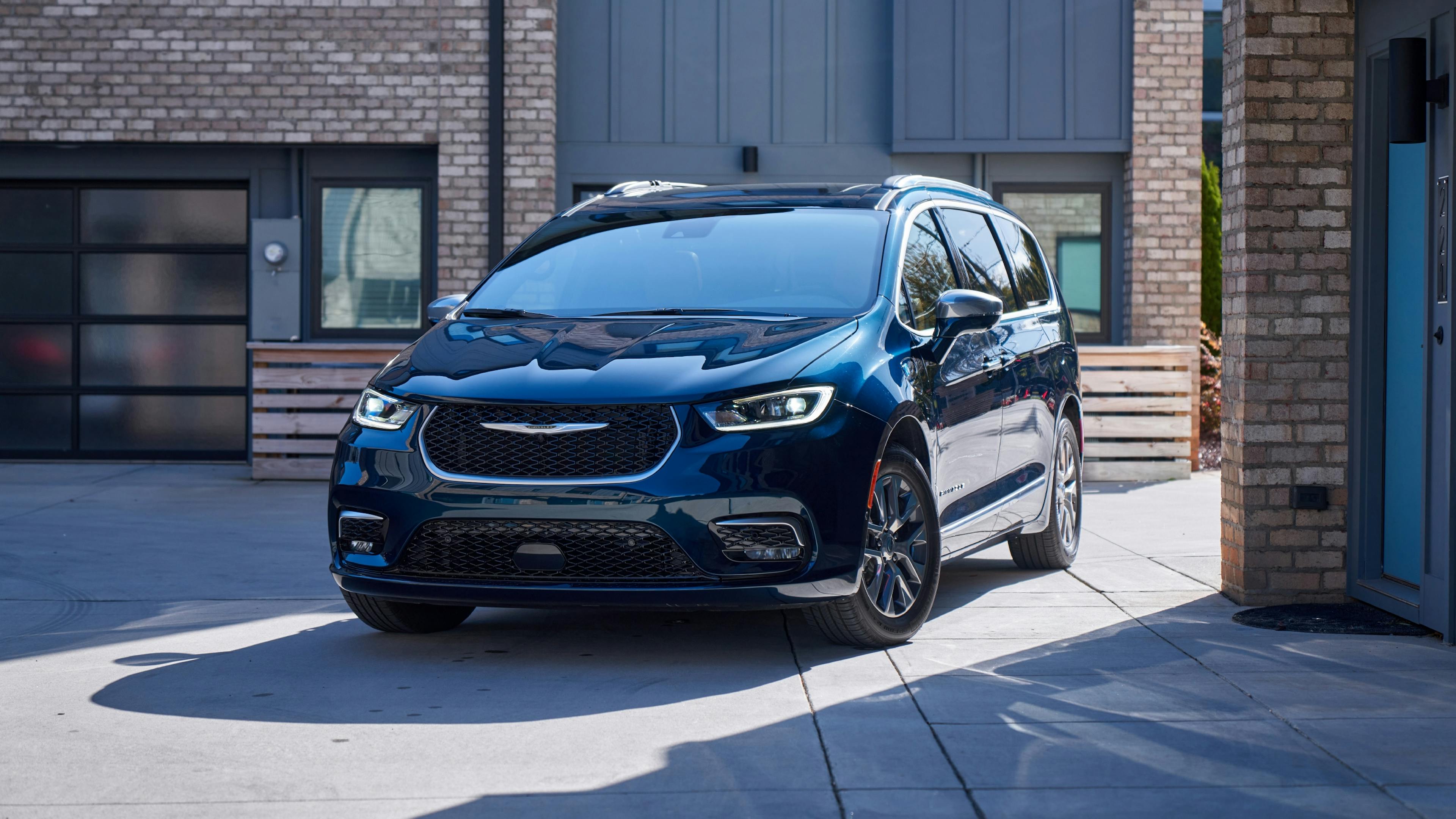 A blue Chrysler Pacifica is parked in front of a modern brick façade.