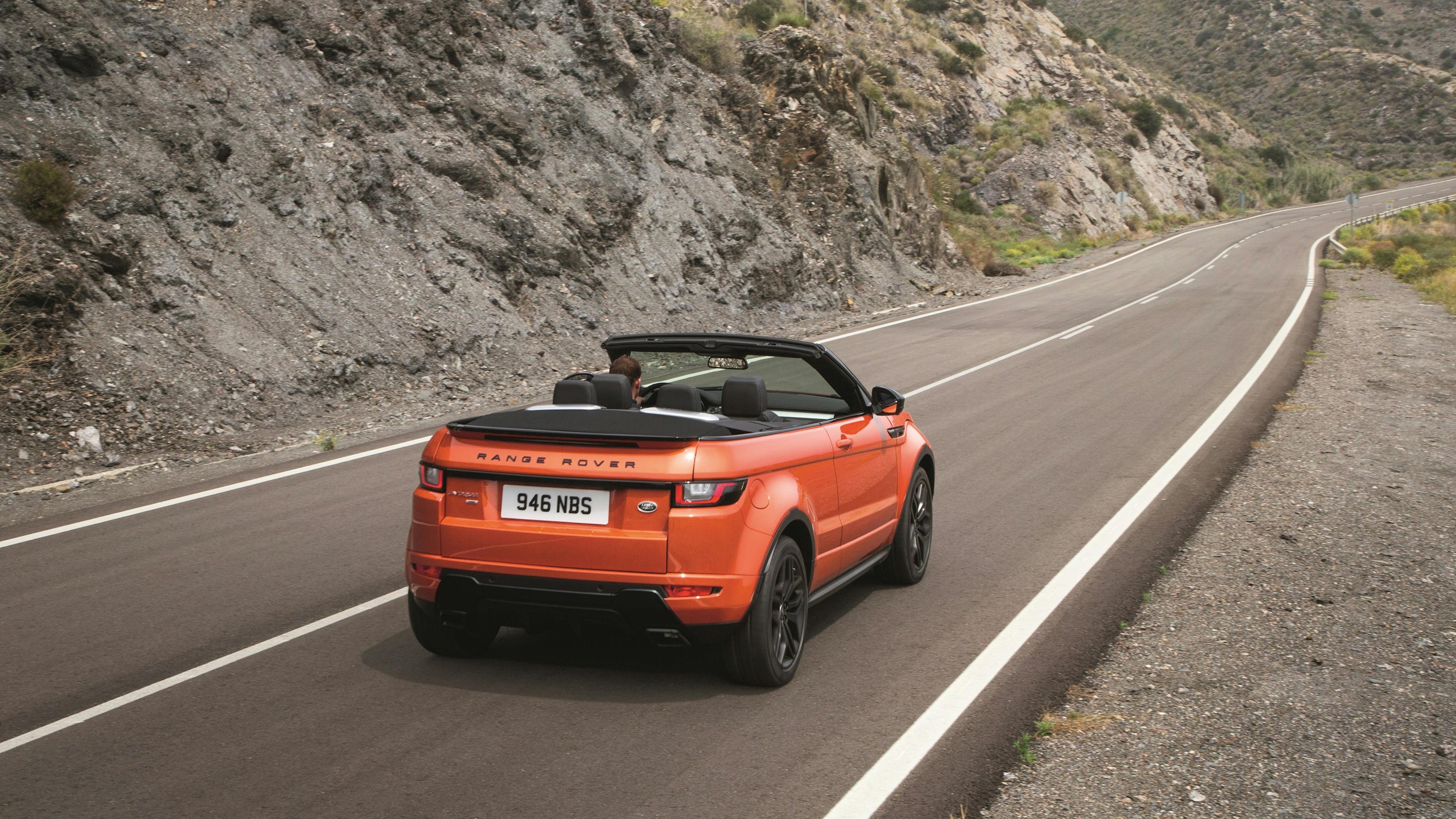 An orange Range Rover Evoque convertible drives on a country road with the top down.