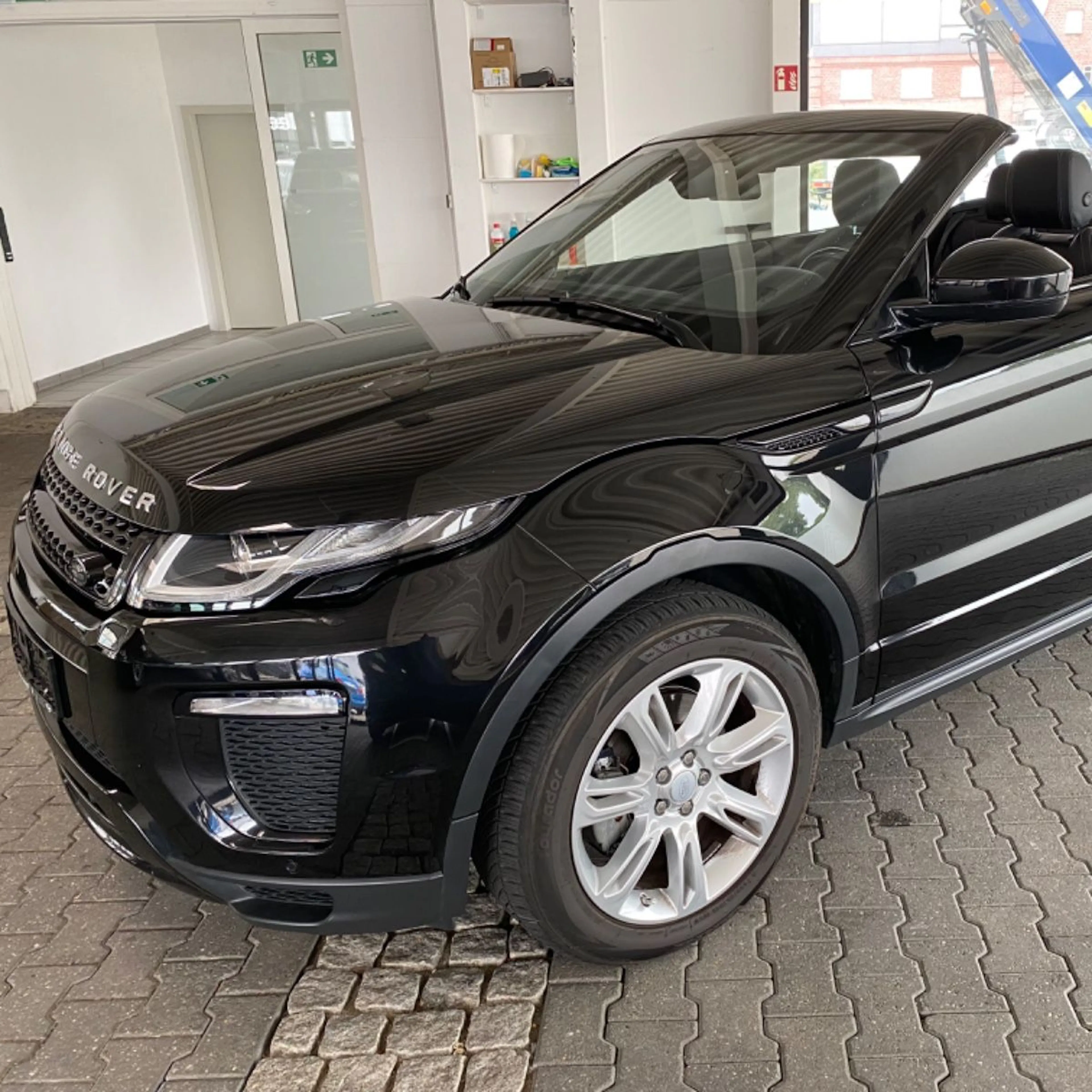 Ein schwarzes Range Rover Evoque Cabriolet mit geöffnetem Dach, seitliche Frontansicht.