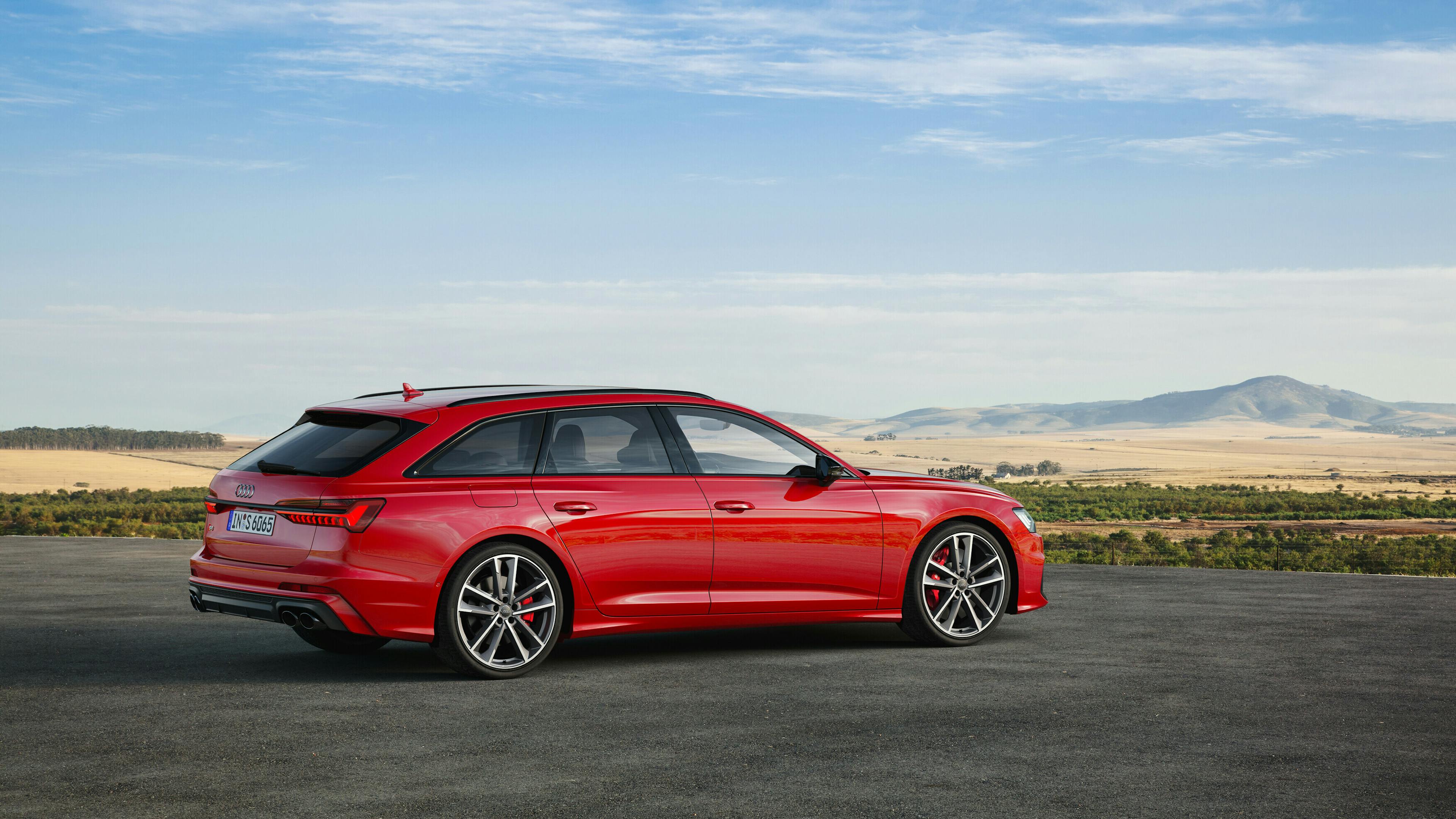 Statische Seitenansicht des roten Audi S6 Avant TDI in einer ländlichen Umgebung mit weitem Horizont im Hintergrund.