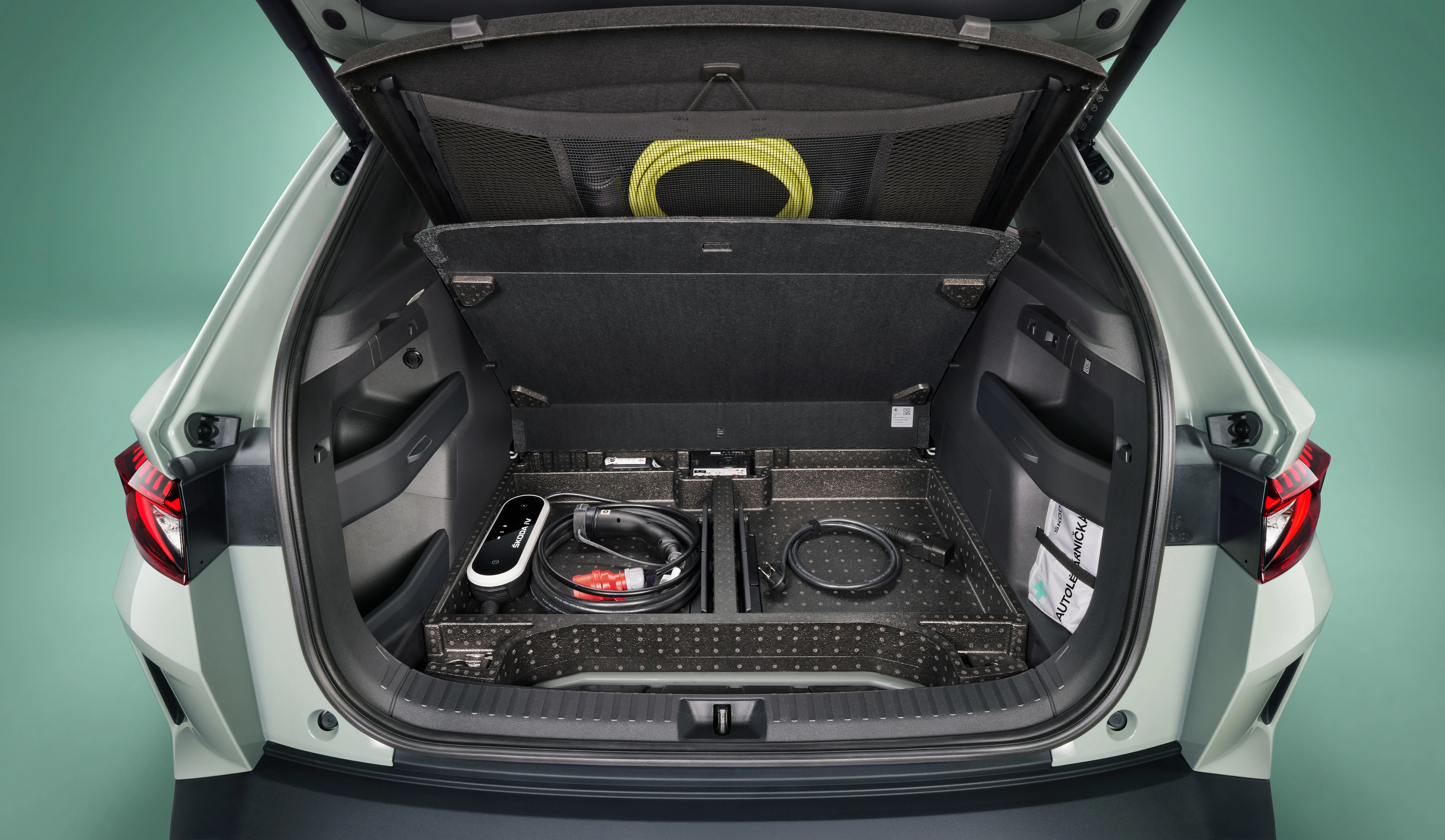 Offener Kofferraum eines Autos mit organisiertem Stauraum, Kabeln und Zubehör, darunter ein Ladekabel für Elektrofahrzeuge.