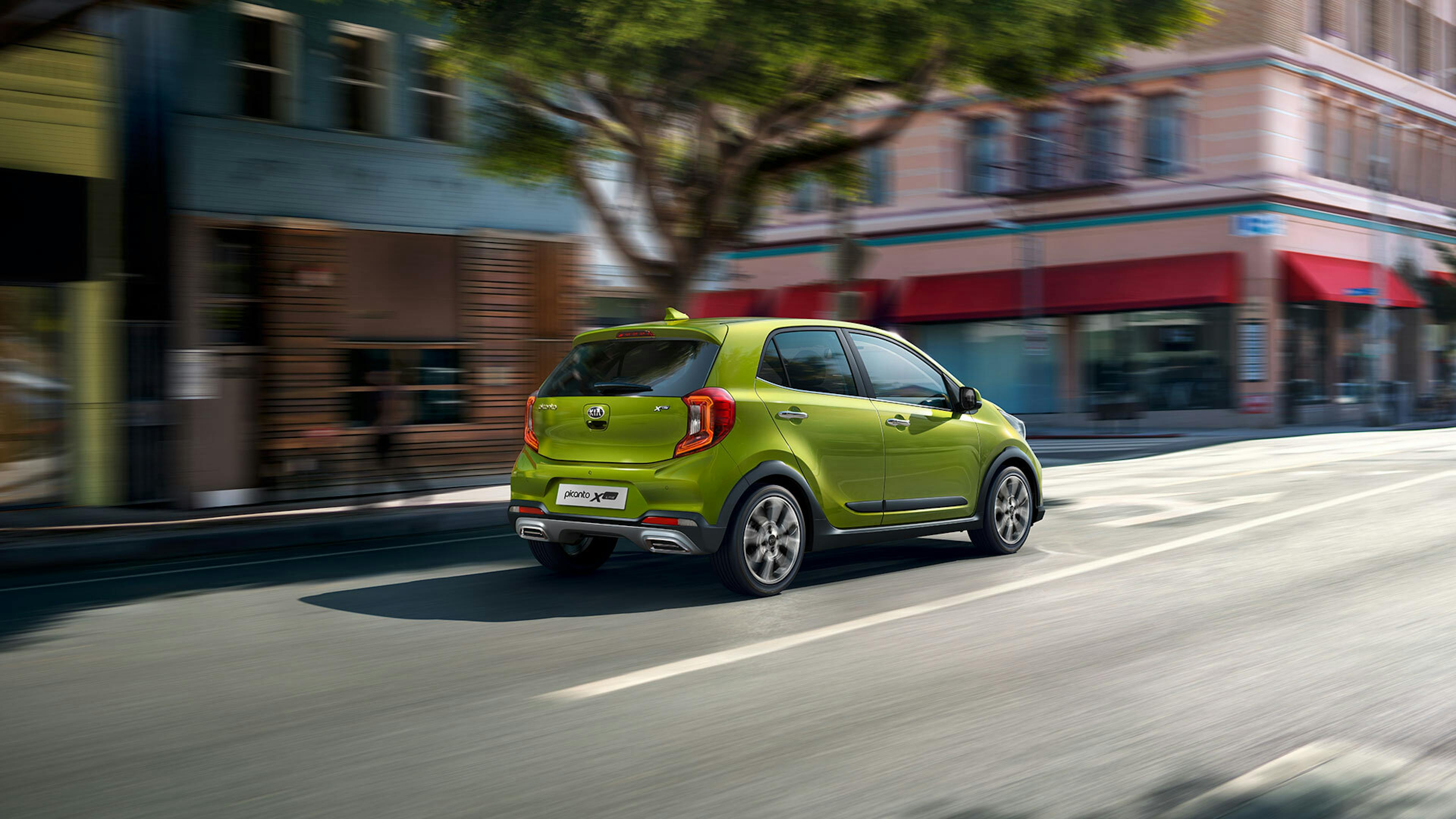 Ein grüner Kia Picanto fährt durch eine belebte Stadtstraße, umgeben von Geschäften.