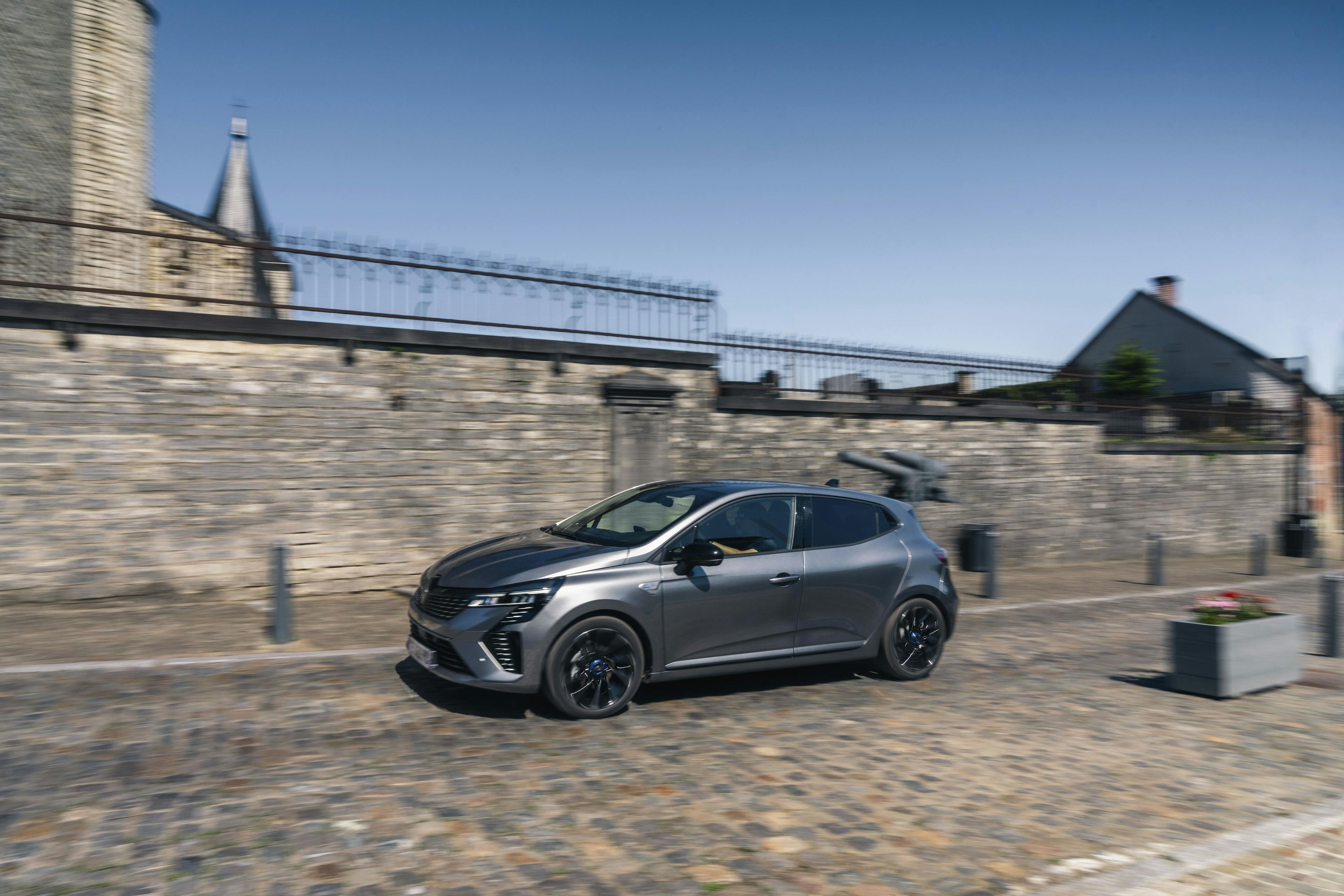  Ein grauer Renault Clio fährt auf einer gepflasterten Straße vor einer historischen Stadtmauer entlang.