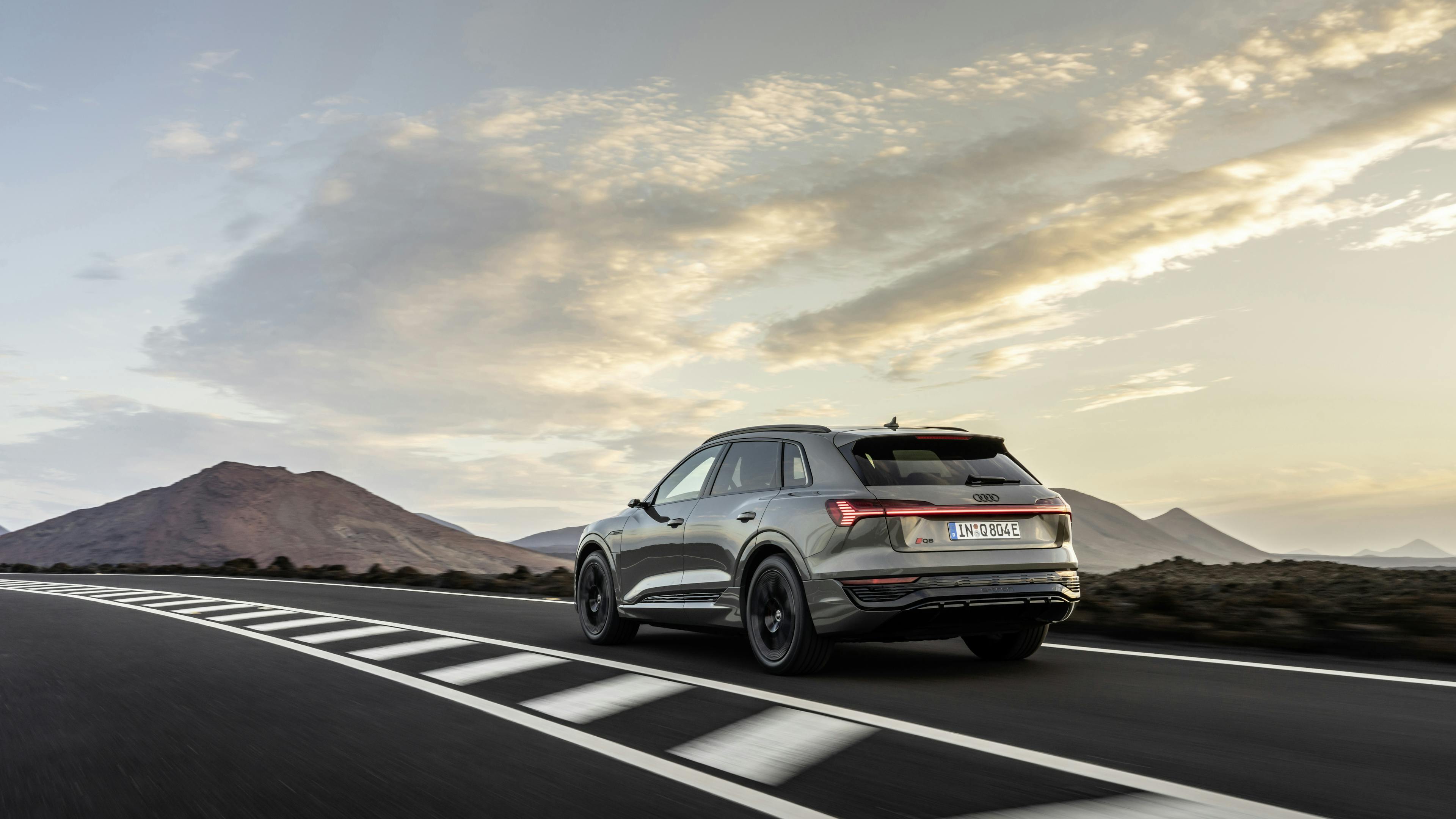 A gray Audi Q8 e-tron is driving on a country road towards the mountains.