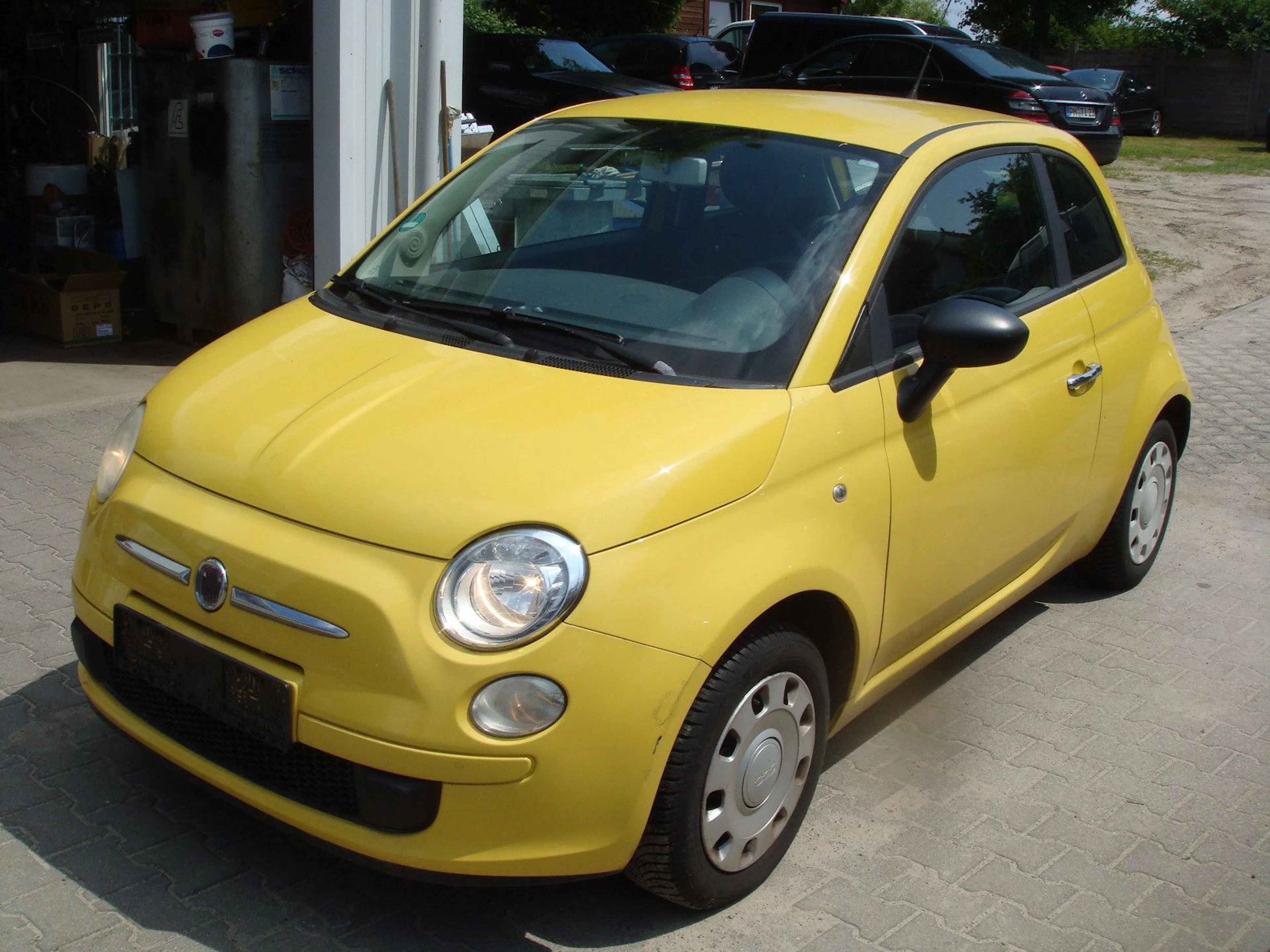 Ein gelber Fiat 500 steht vor einer Werkstatt
