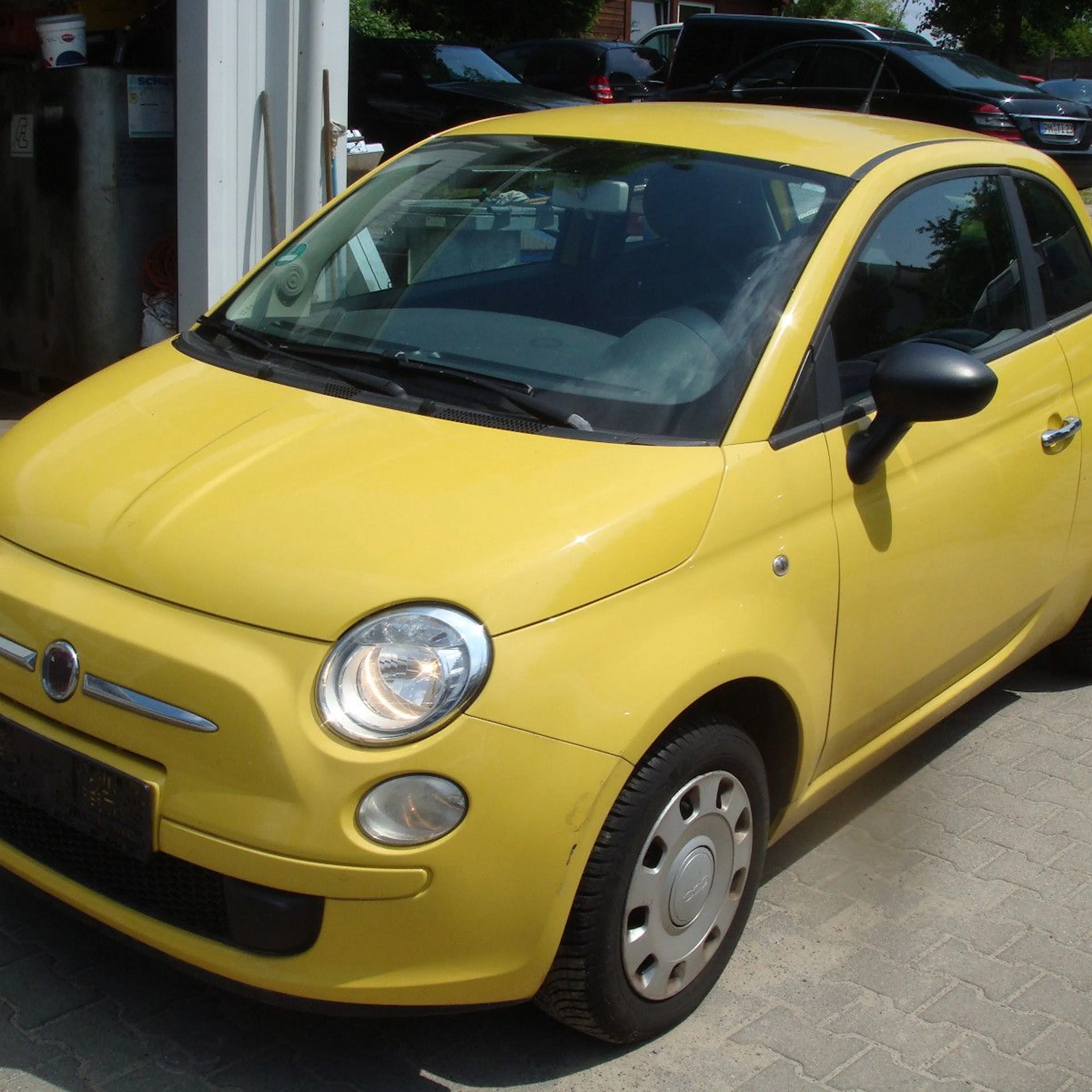 Ein gelber Fiat 500 steht vor einer Werkstatt