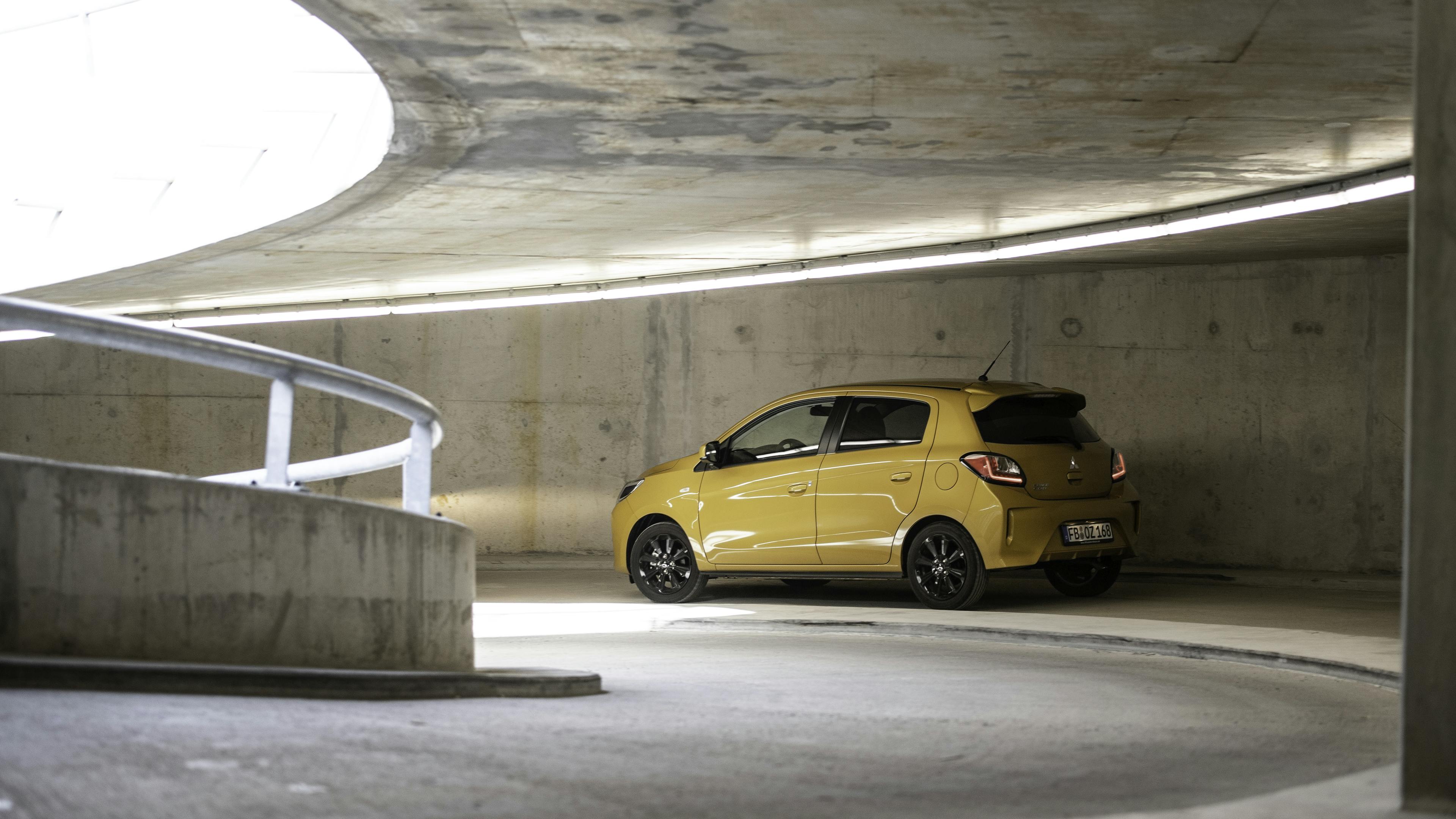 A yellow Mitsubishi Space Star drives through a parking garage.