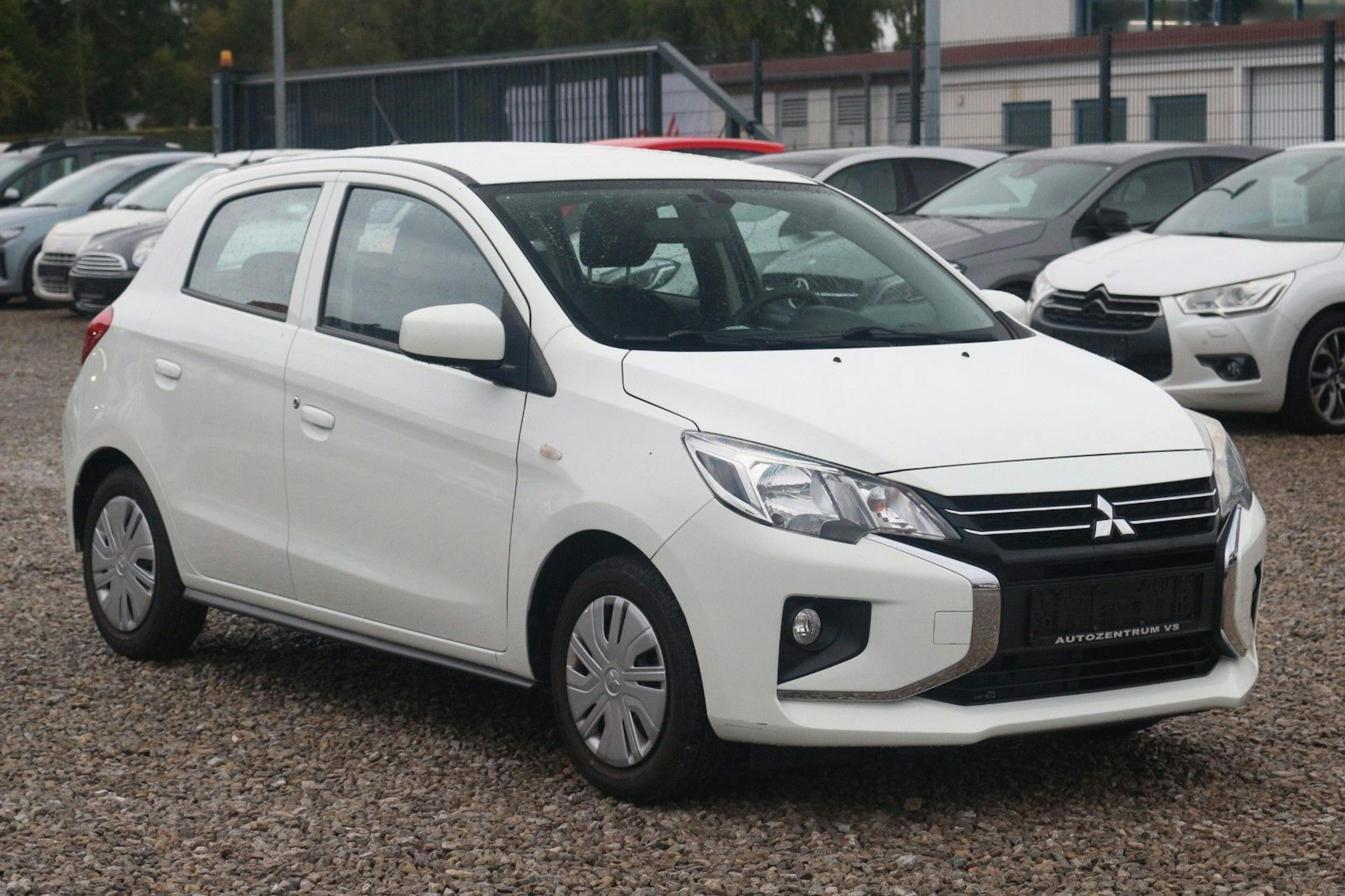  Ein weißer Mitsubishi Space Star steht auf einem Kiesplatz.