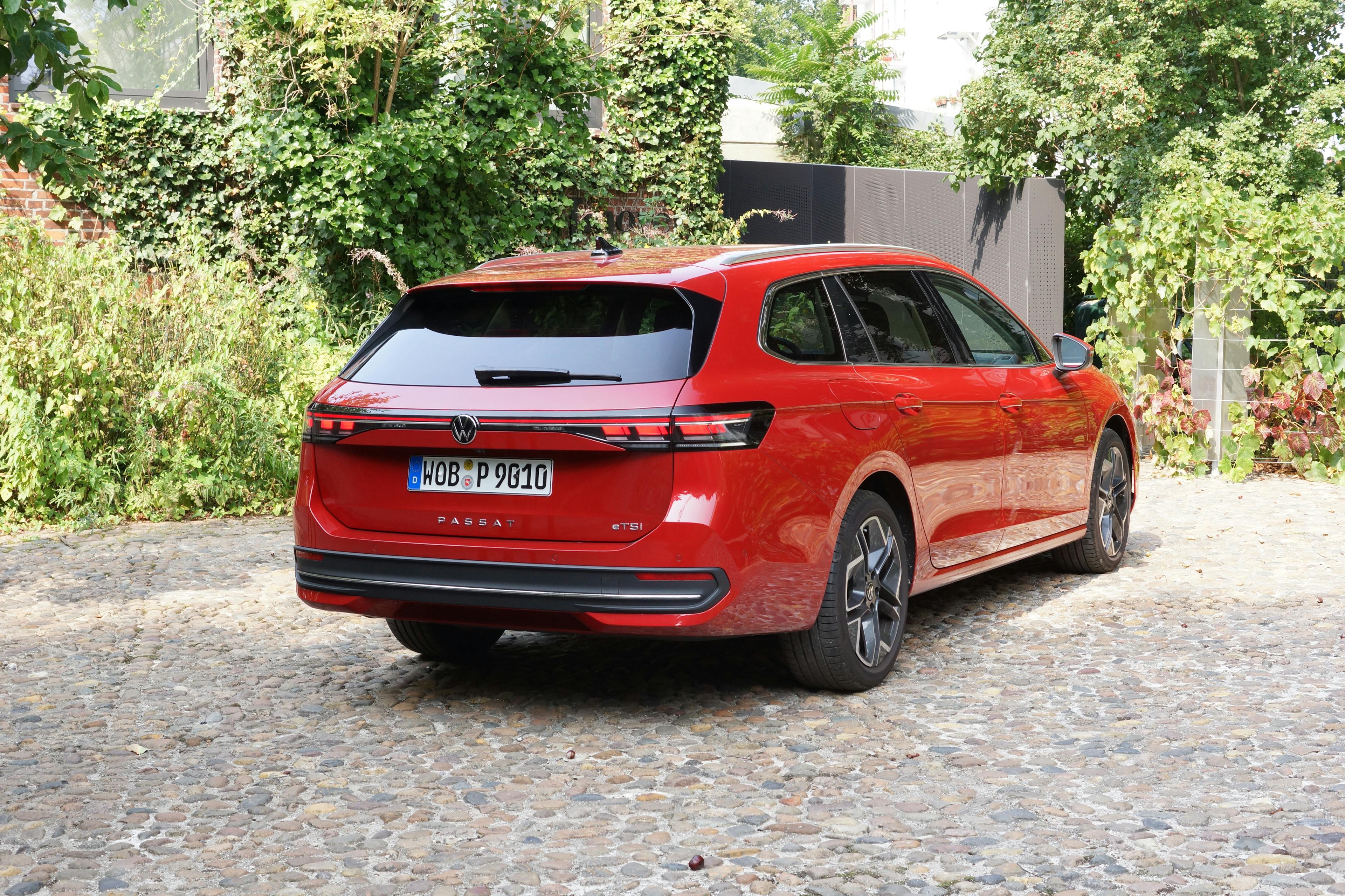 Ein roter VW Passat B9 auf einem Kopfsteinpflasterplatz mit Klinkergebäude im Hintergrund.