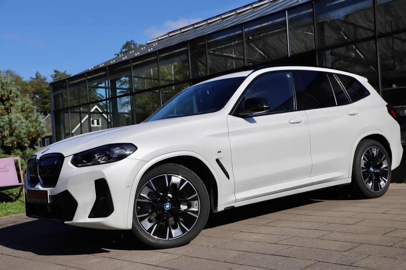 Ein weißer BMW iX3 steht vor einem Autohaus.