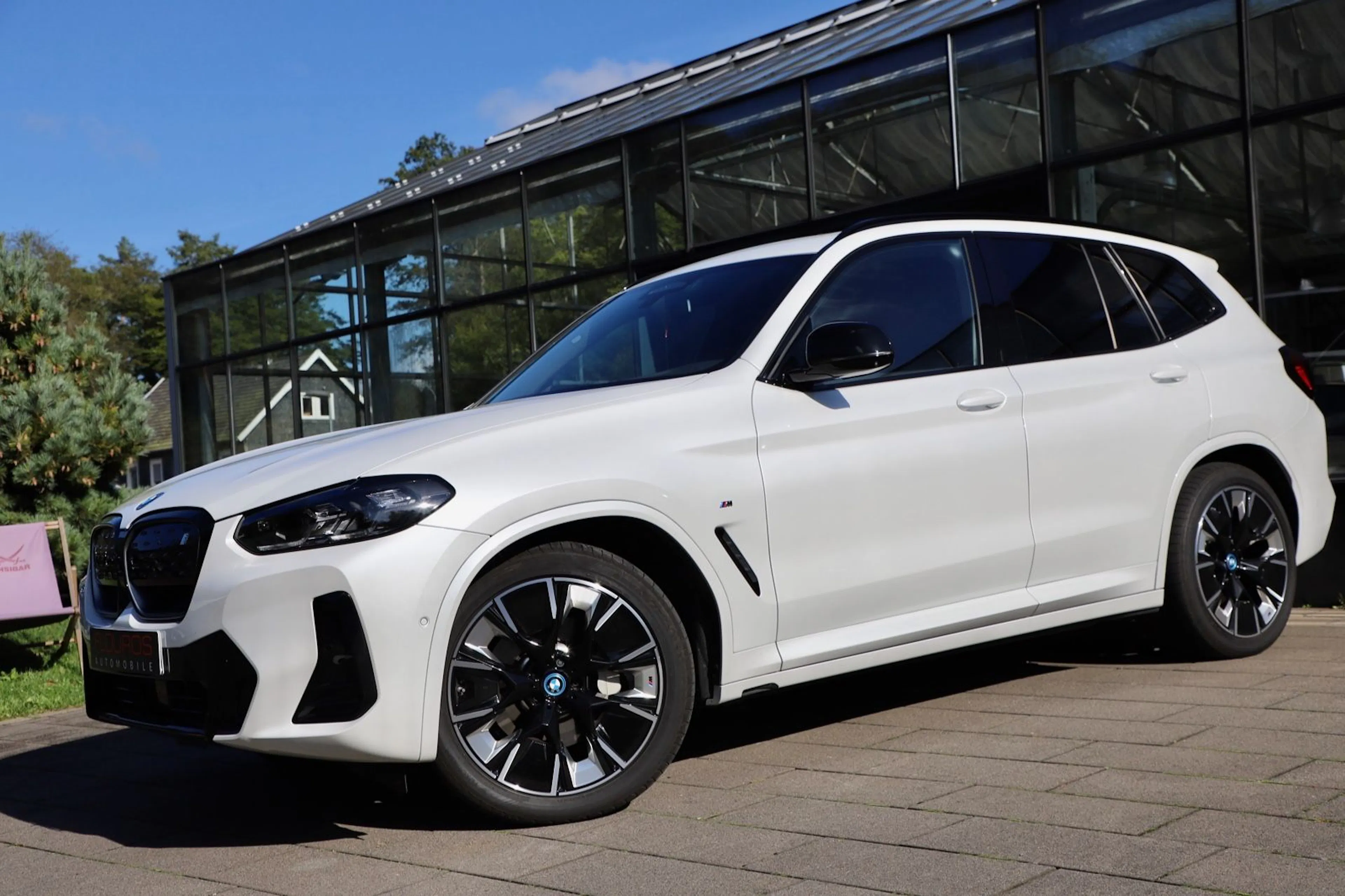 Ein weißer BMW iX3 steht vor einem Autohaus.