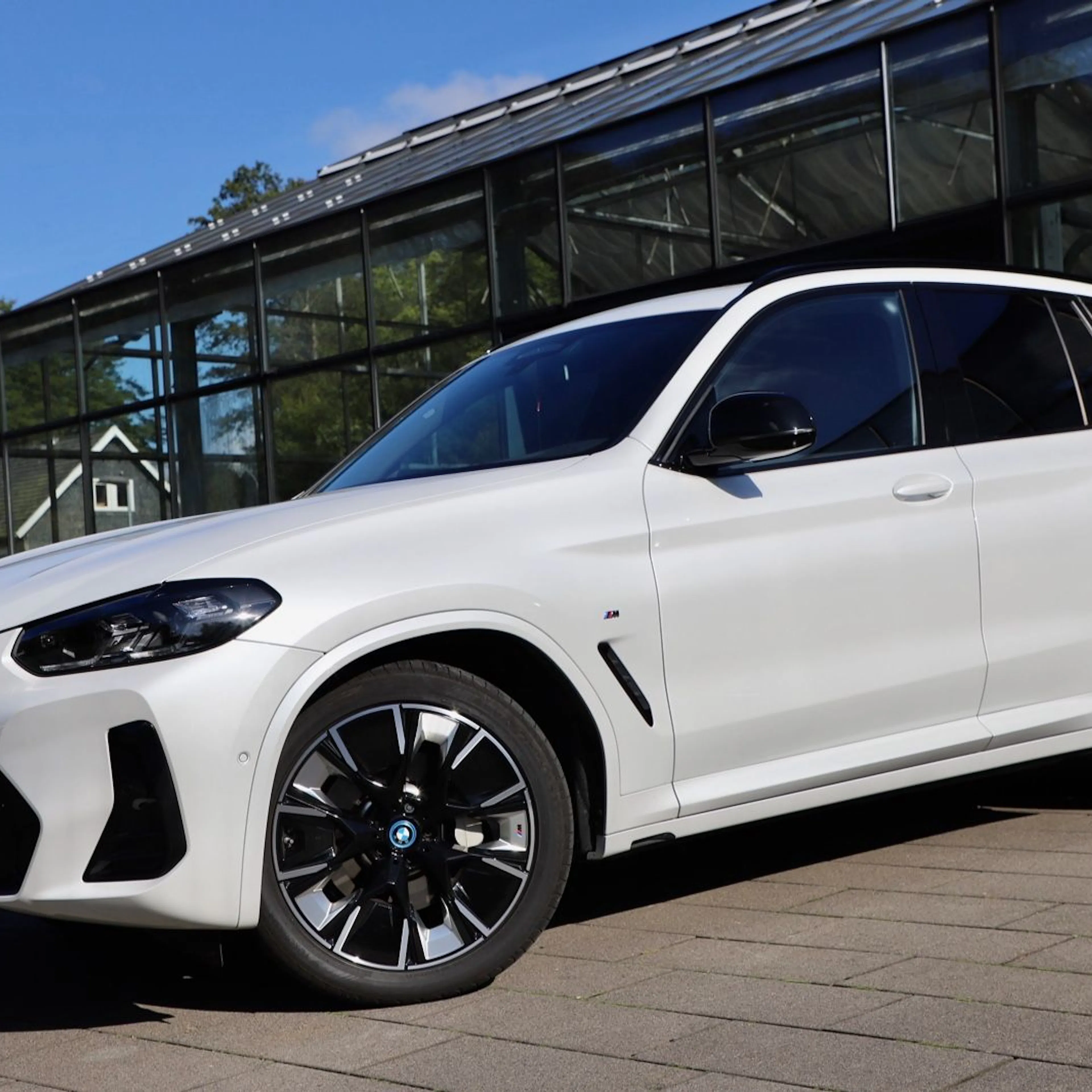 Ein weißer BMW iX3 steht vor einem Autohaus.