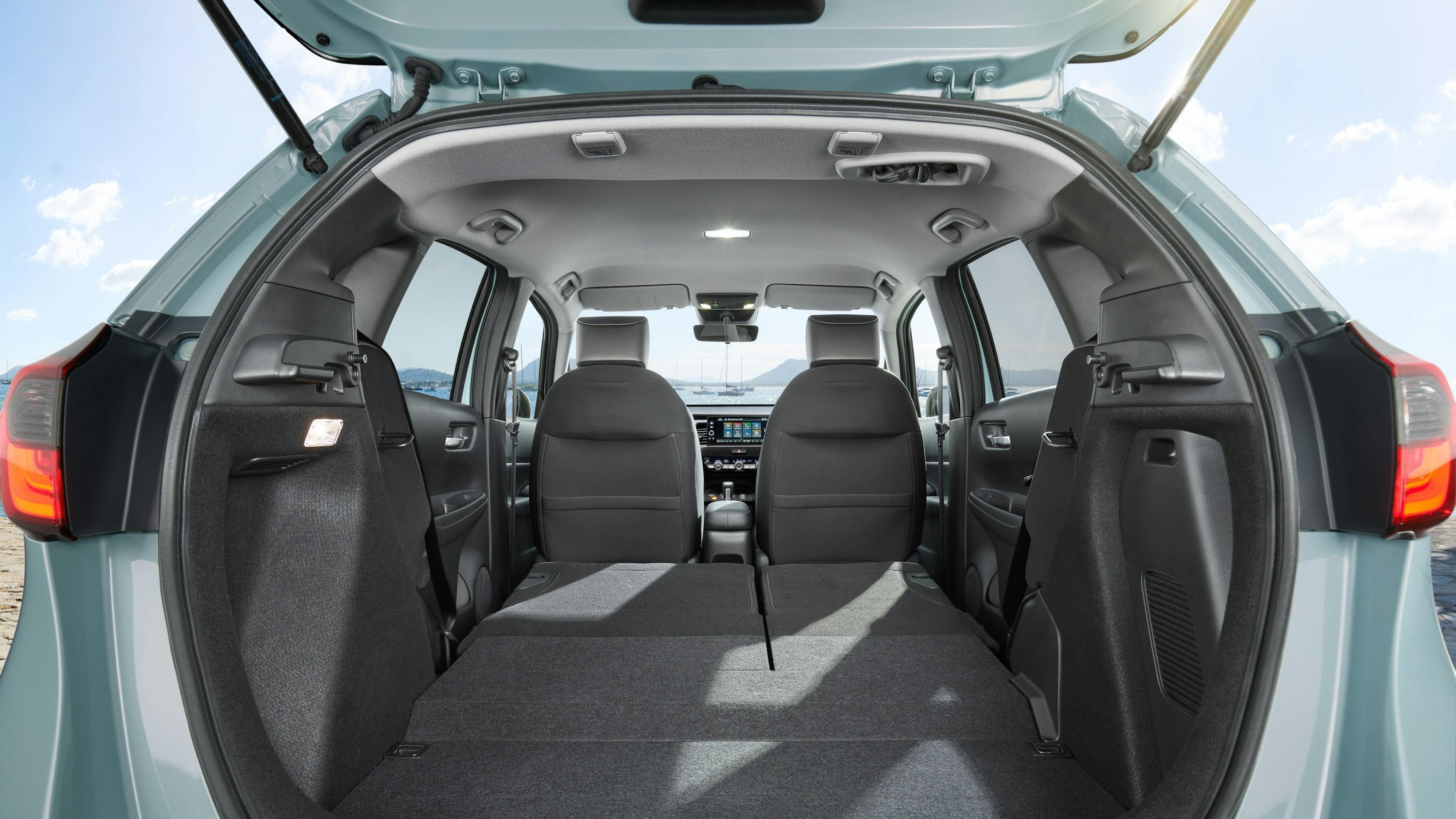 View into the spacious trunk of an open Honda Jazz with the rear seats folded down, taken in daylight with a view of a landscape in the background.