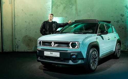 Ein Mann lehnt an einem hellblauen Renault R4 E-Tech Electric, der in einer industriellen Umgebung präsentiert wird.