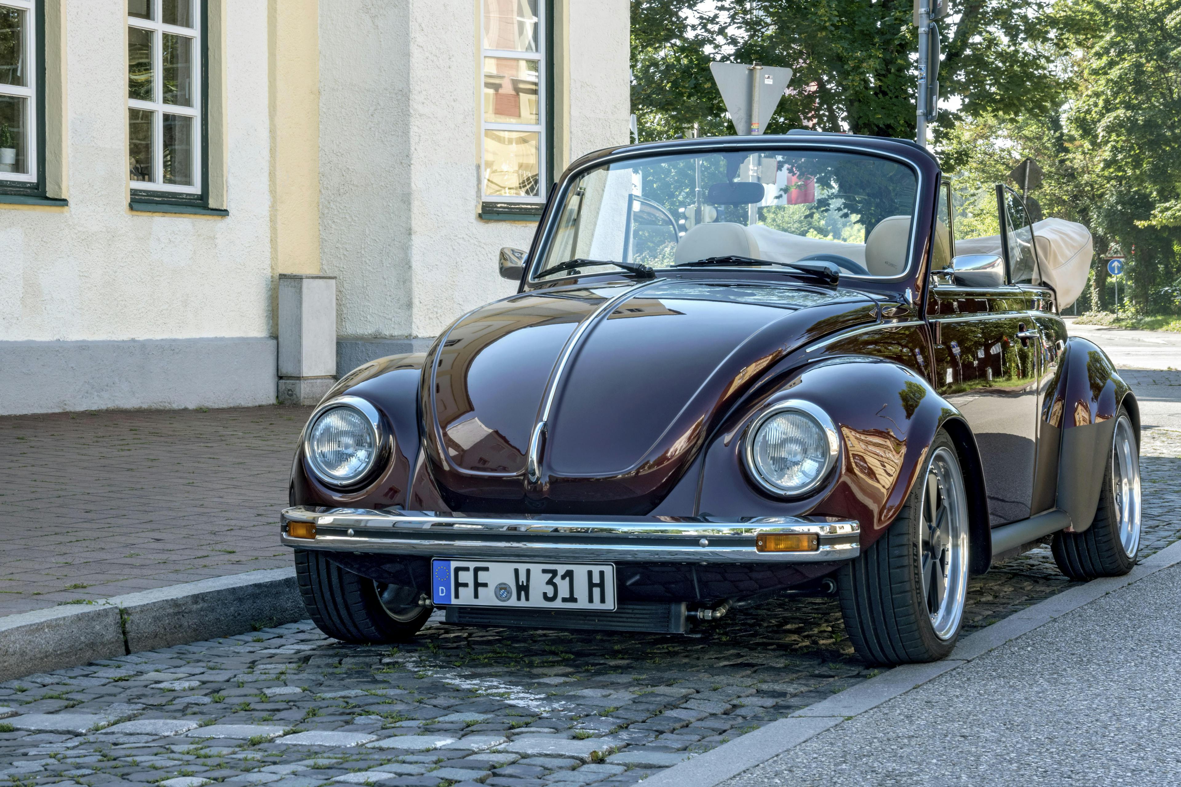 Ein VW Käfer Cabriolet mit H-Kennzeichen parkt am Straßenrand vor einem Gebäude.