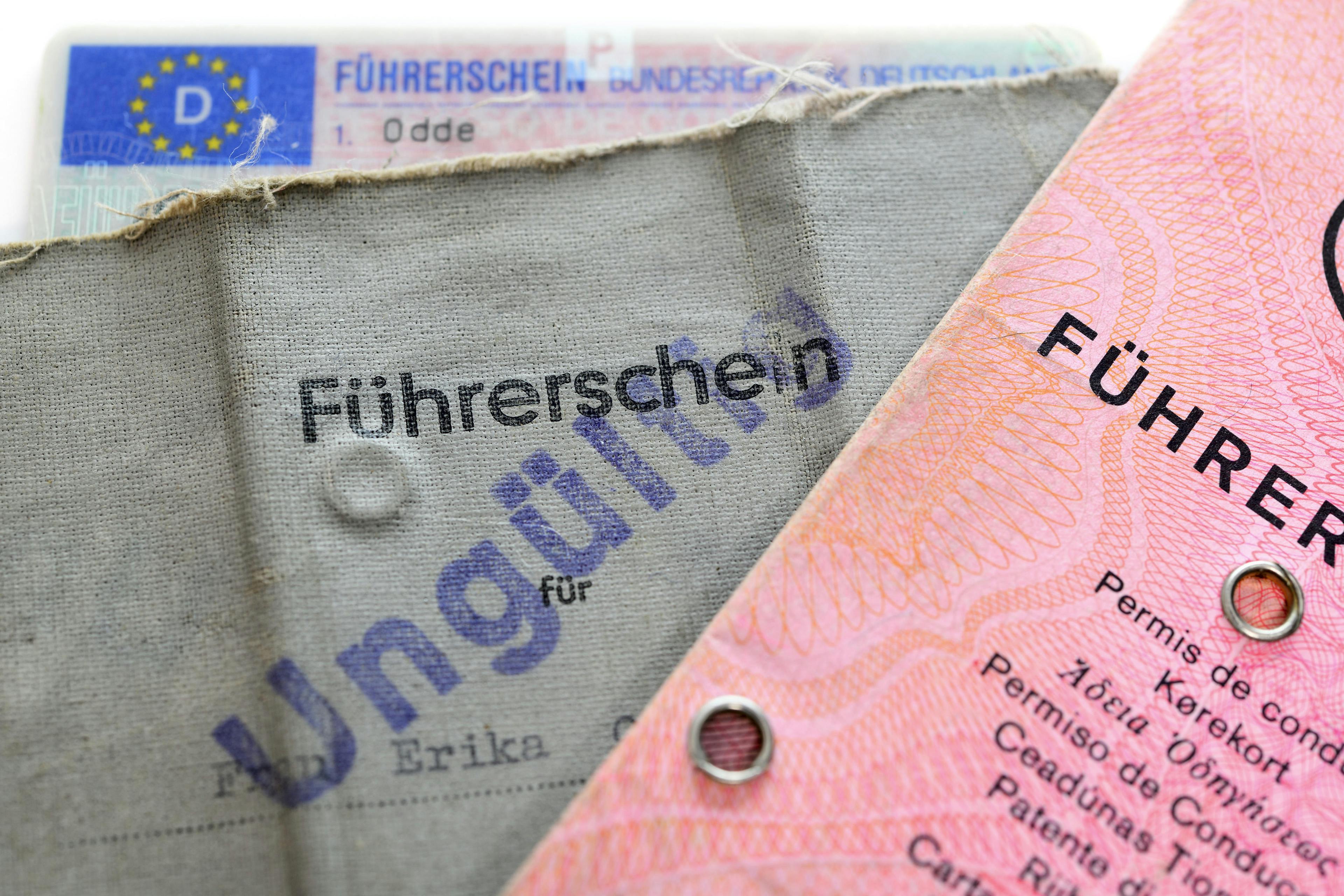  Abgebildet sind mehrere Führerscheine, darunter ein ungültig gestempelter grauer Papierführerschein und ein rosafarbener Führerschein im klassischen Design.