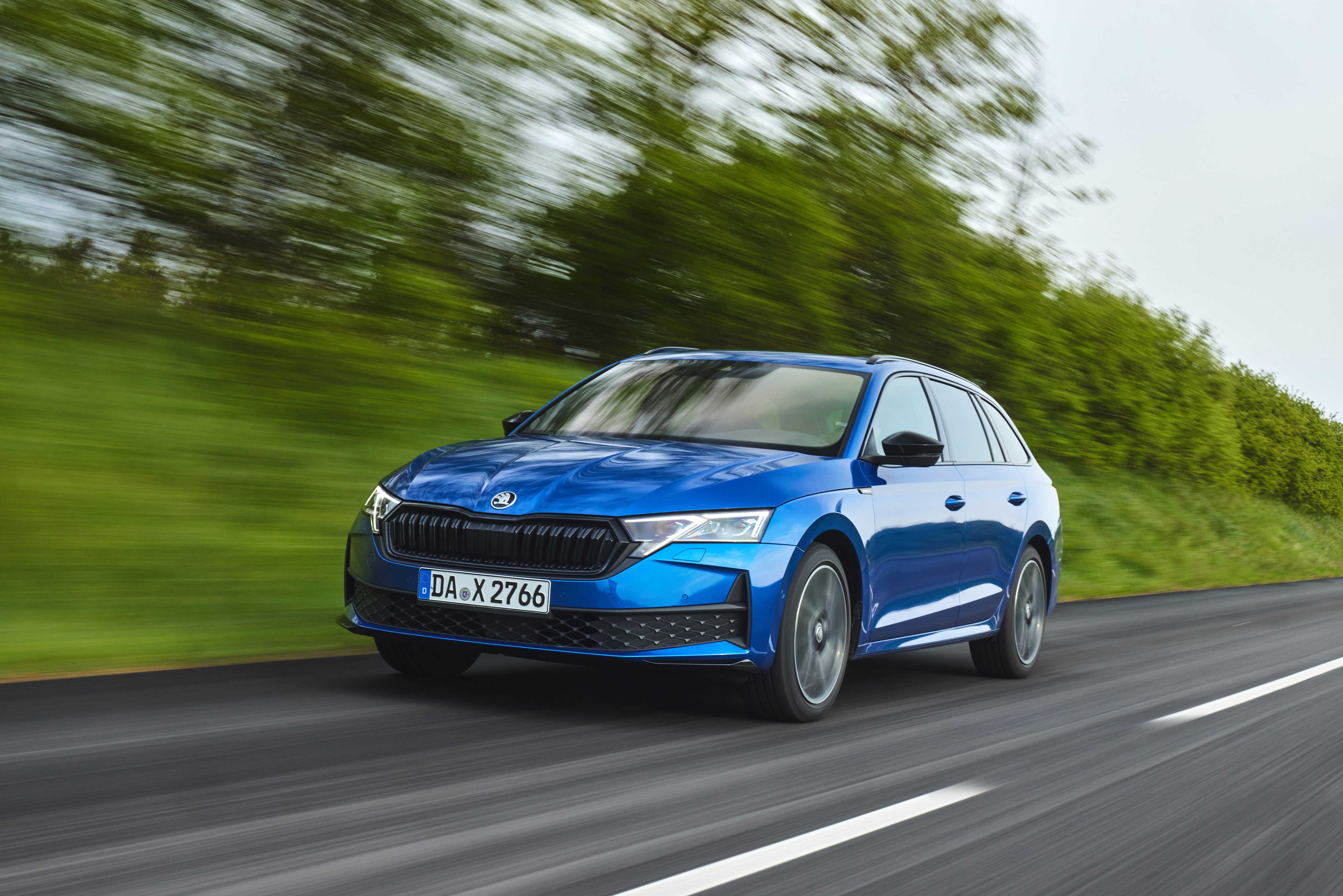 Blauer Škoda Octavia Combi fährt auf einer Landstraße vor grünen Bäumen.