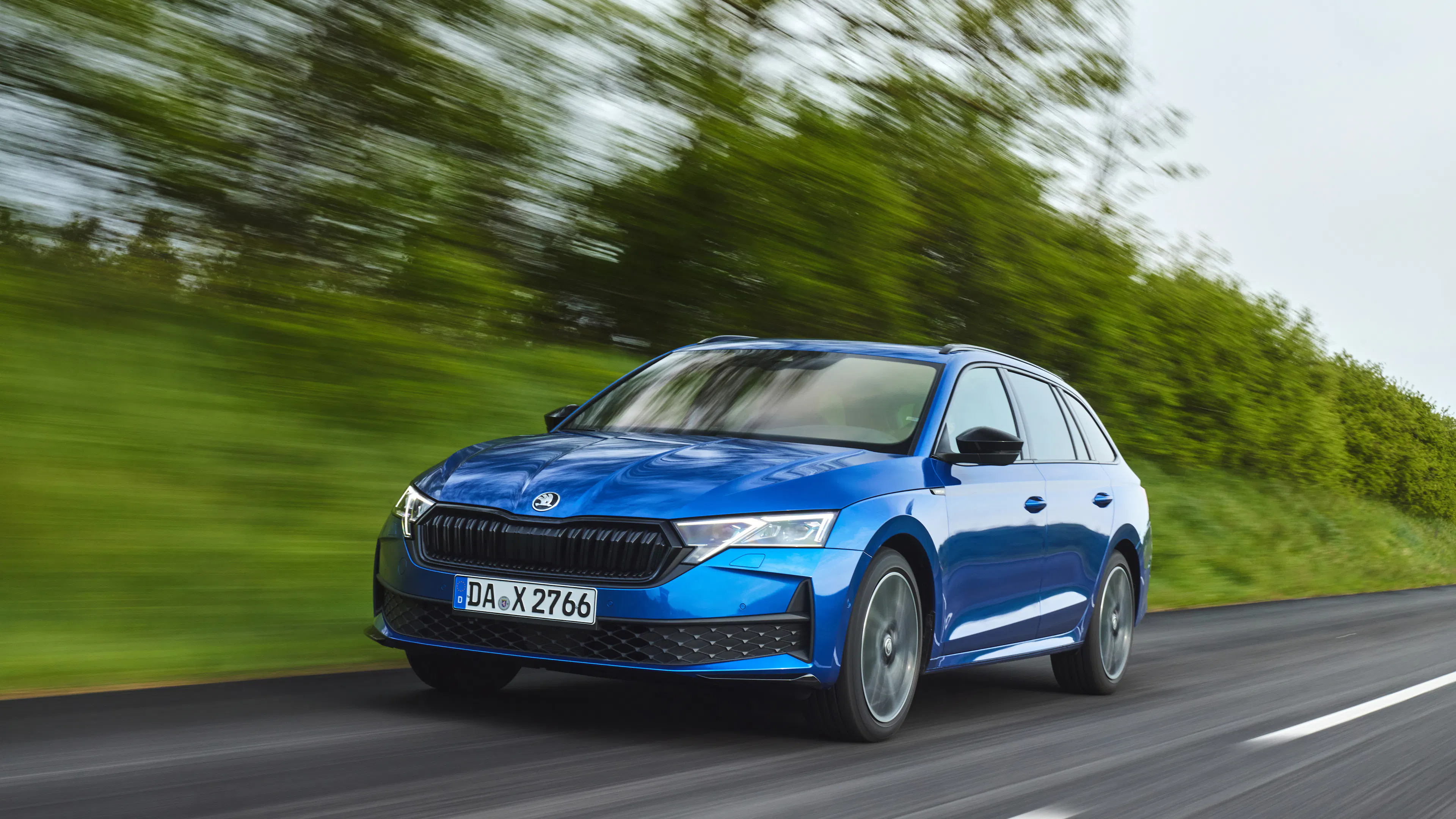 Blauer Škoda Octavia Combi fährt auf einer Landstraße vor grünen Bäumen.