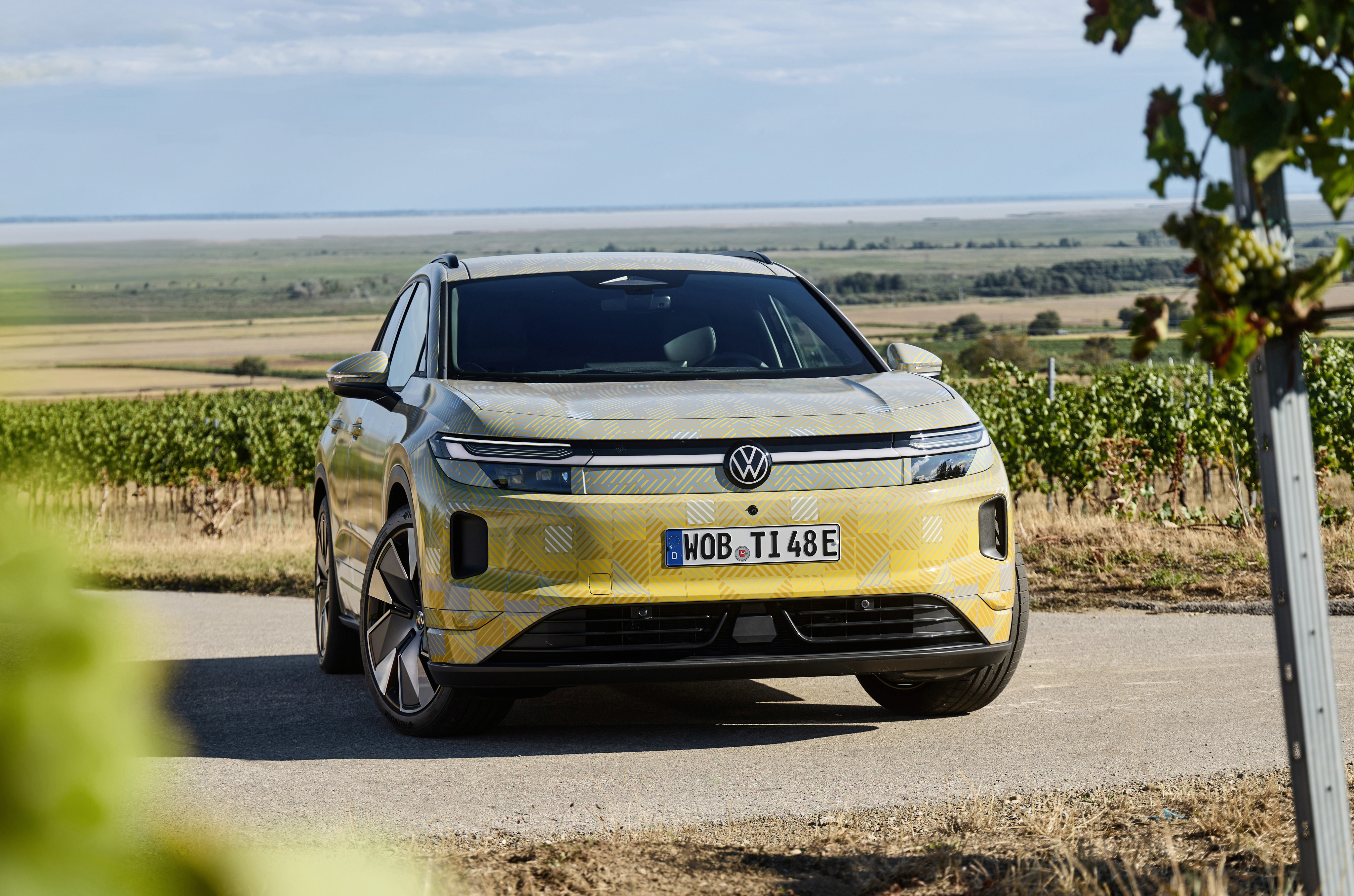 VW ID.Tiguan mit Tarnfolie steht vor Weinbergen, Frontansicht.
