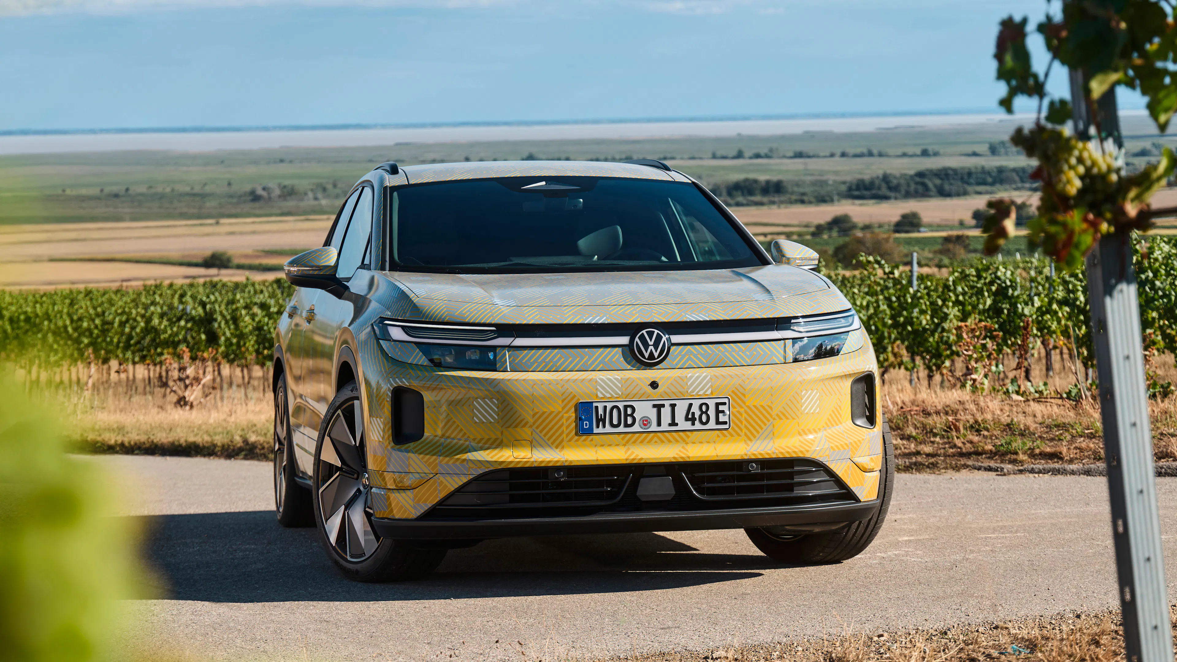 VW ID.Tiguan mit Tarnfolie steht vor Weinbergen, Frontansicht.