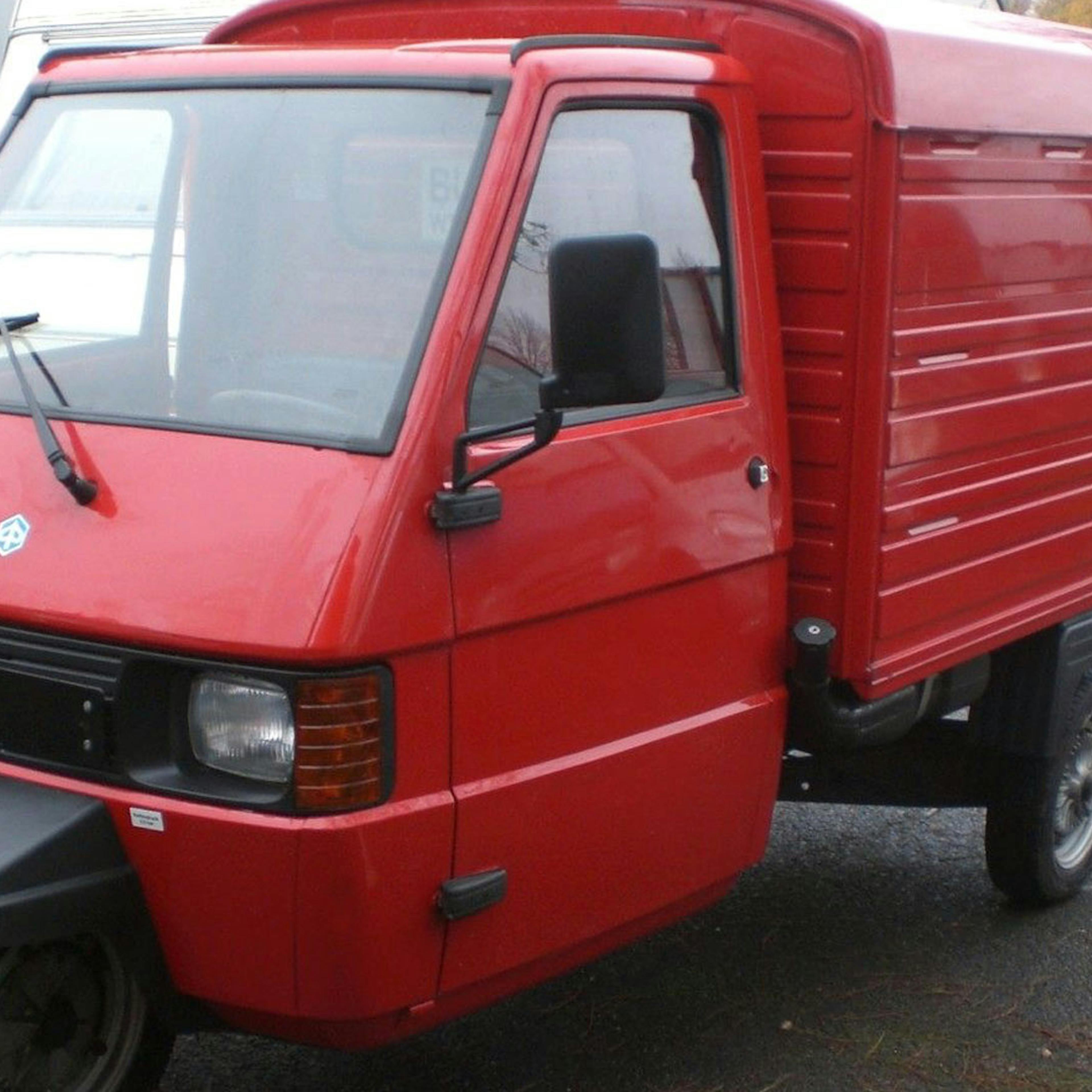 Ein rotes Piaggio Ape Microcar steht auf einem Parkplatz.