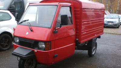 Ein rotes Piaggio Ape Microcar steht auf einem Parkplatz.