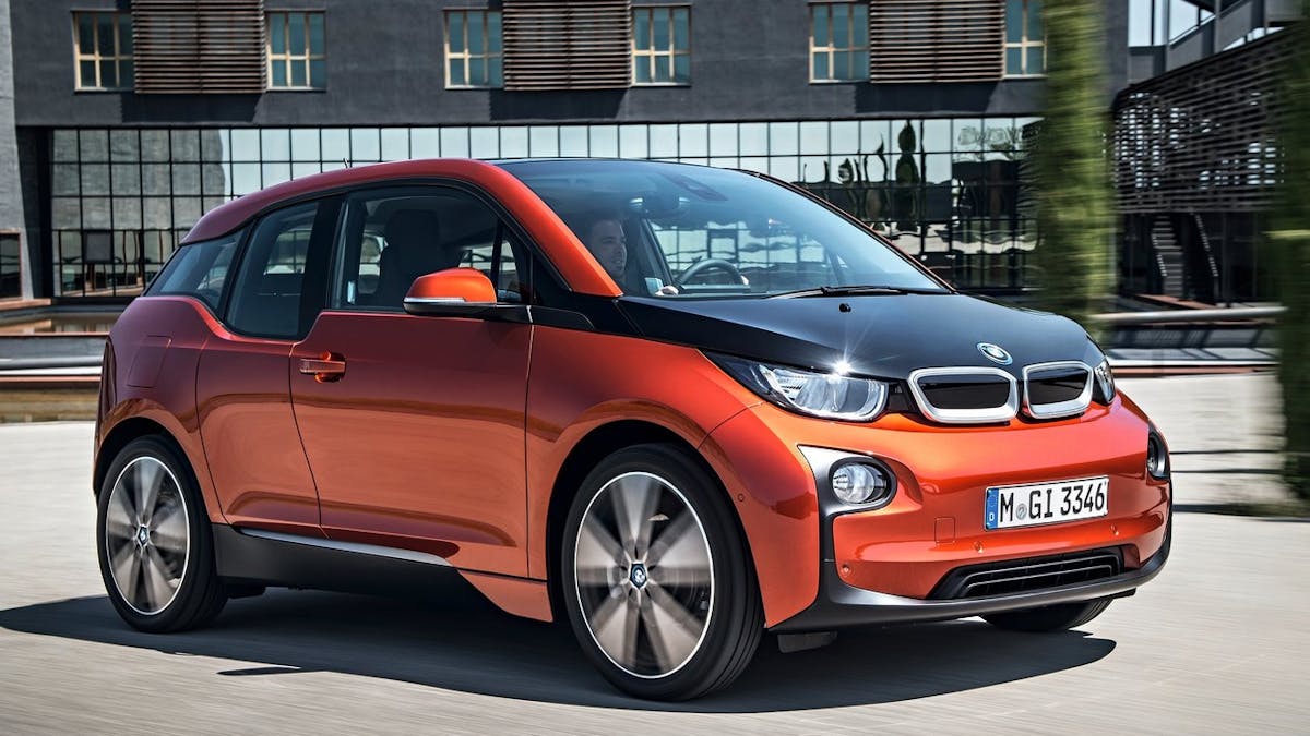 Ein oranger BMW i3 fährt vor einem Gebäude entlang.