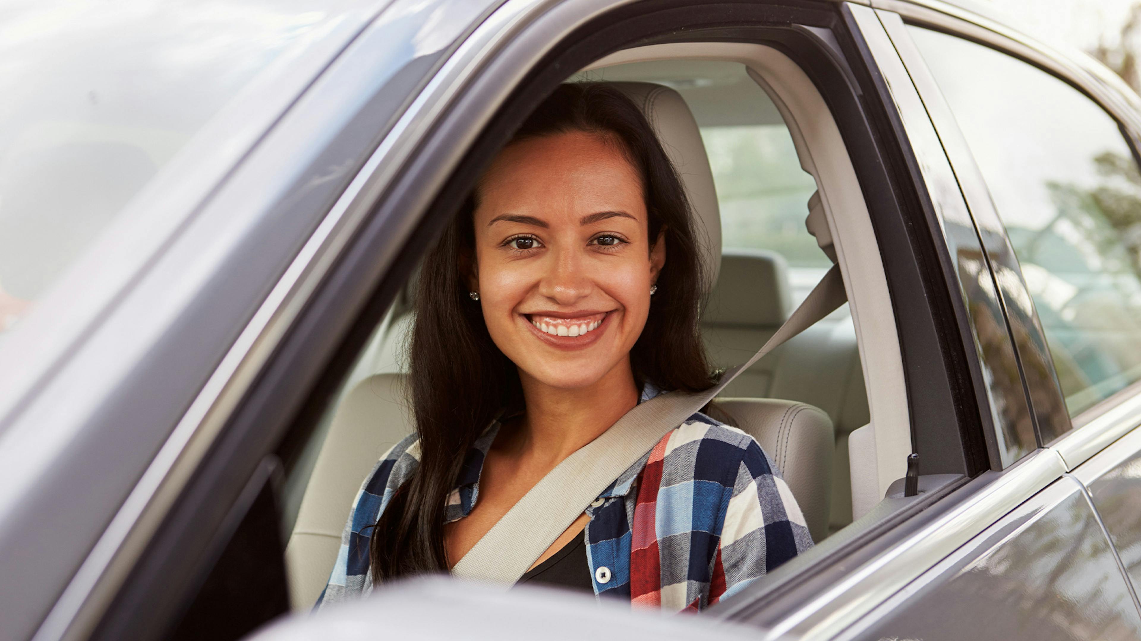 Eine junge Frau sitzt lachend auf dem Fahrersitz eines grauen Pkw.