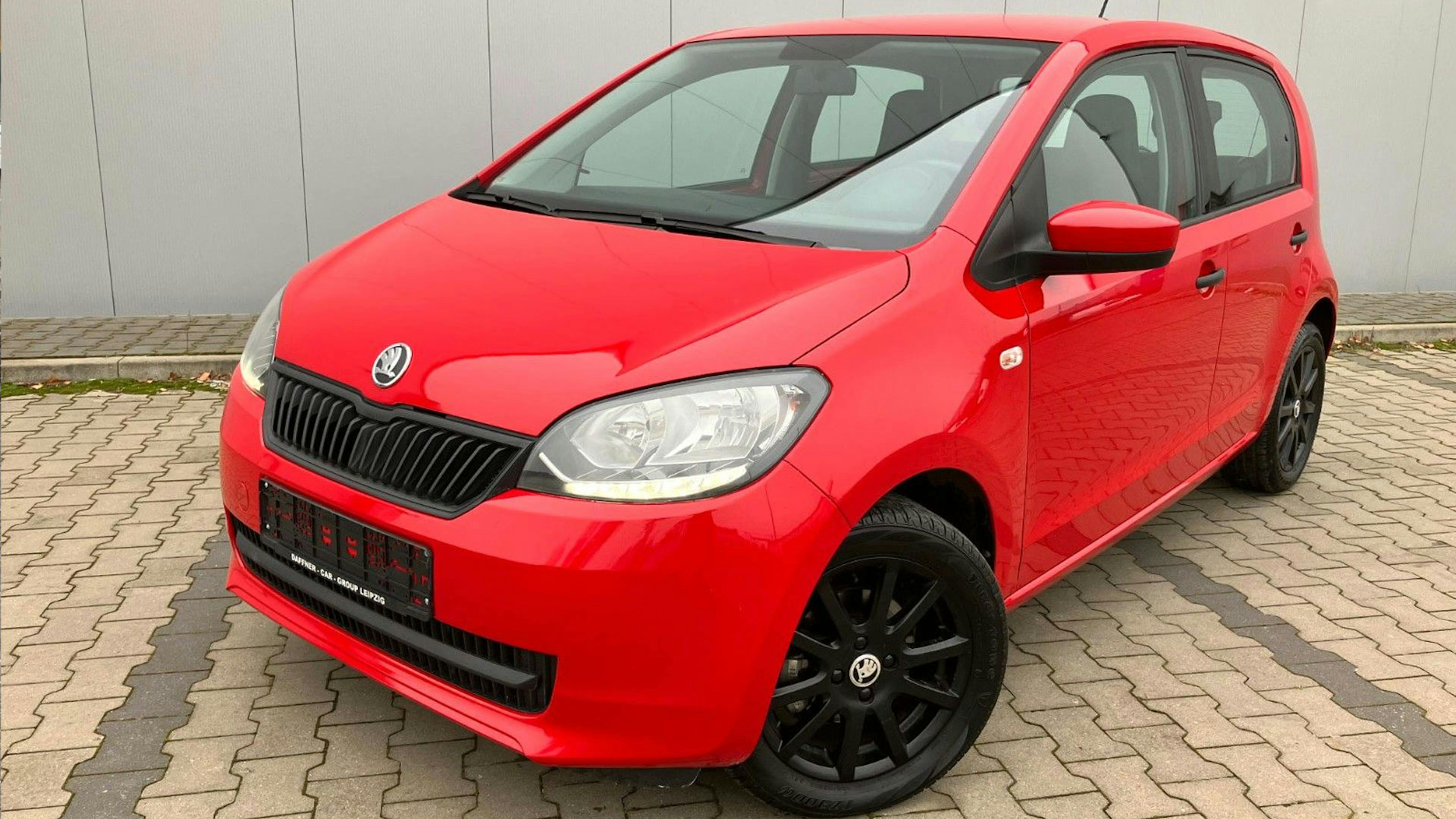 Ein roter Škoda-Citigo-Kleinstwagen steht vor einem grauen Gebäude.