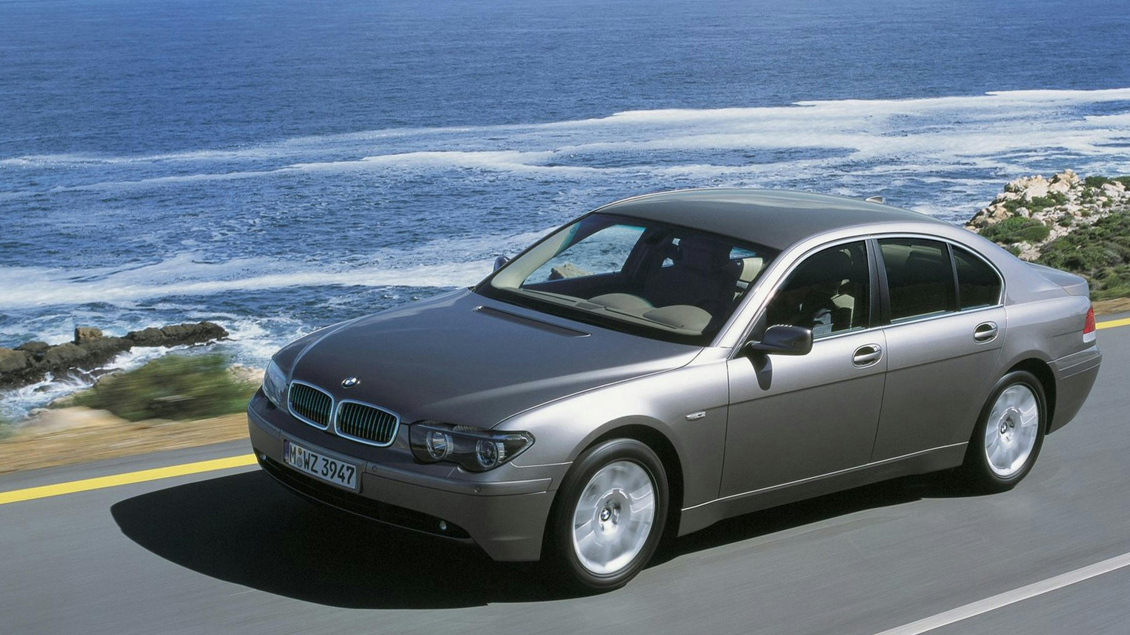 Ein silberner BMW 7er fährt eine Küstenstraße entlang.