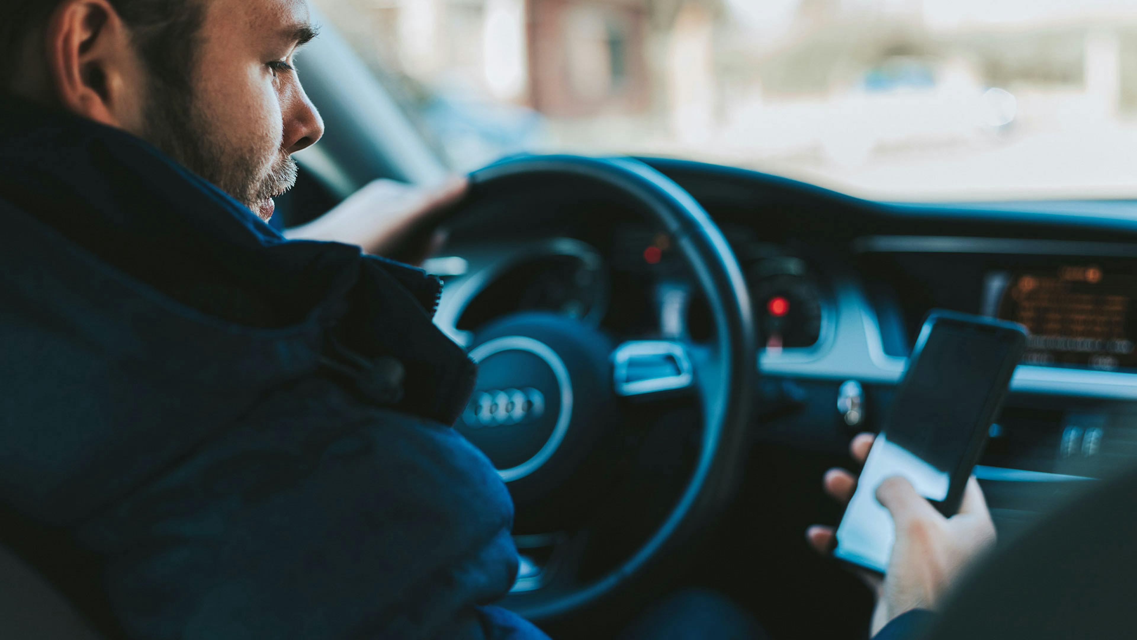 Ein Mann sitzt am Steuer eines Pkw und benutzt ein Smartphone
