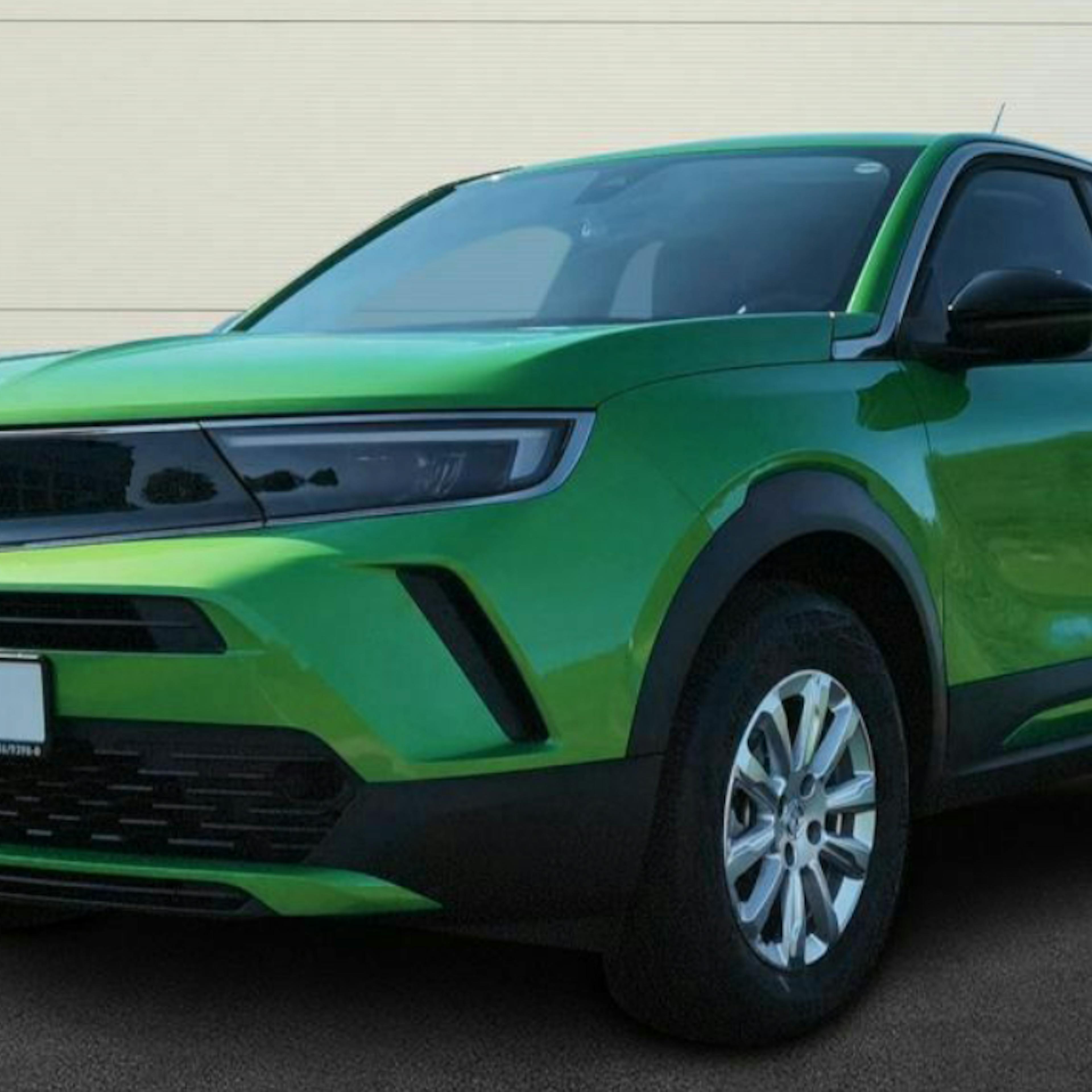Ein grüner Opel Mokka-e steht vor einer hellen Wand.