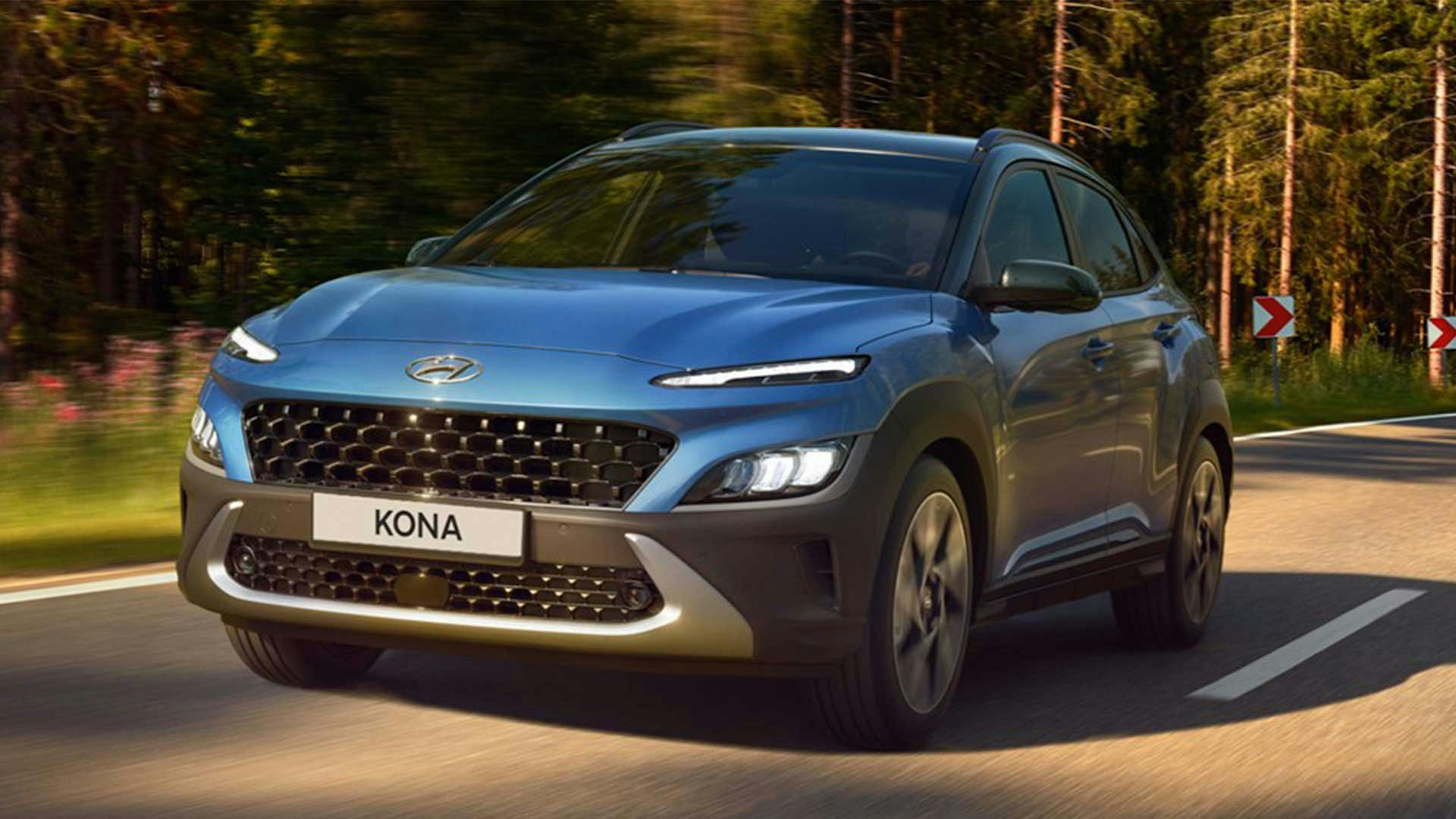 Ein blauer Hyundai Kona Select Hybrid fährt eine Landstraße entlang.
