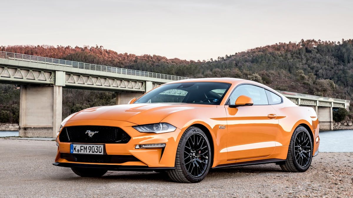 Ein oranger Ford Mustang GT steht an einem Flussufer