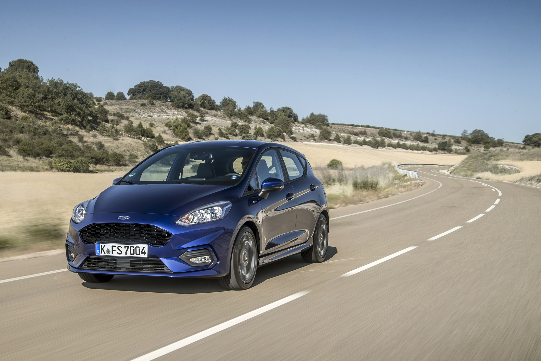 Ein blauer Ford Fiesta fährt in einer kargen Landschaft auf einer kurvigen Straße.