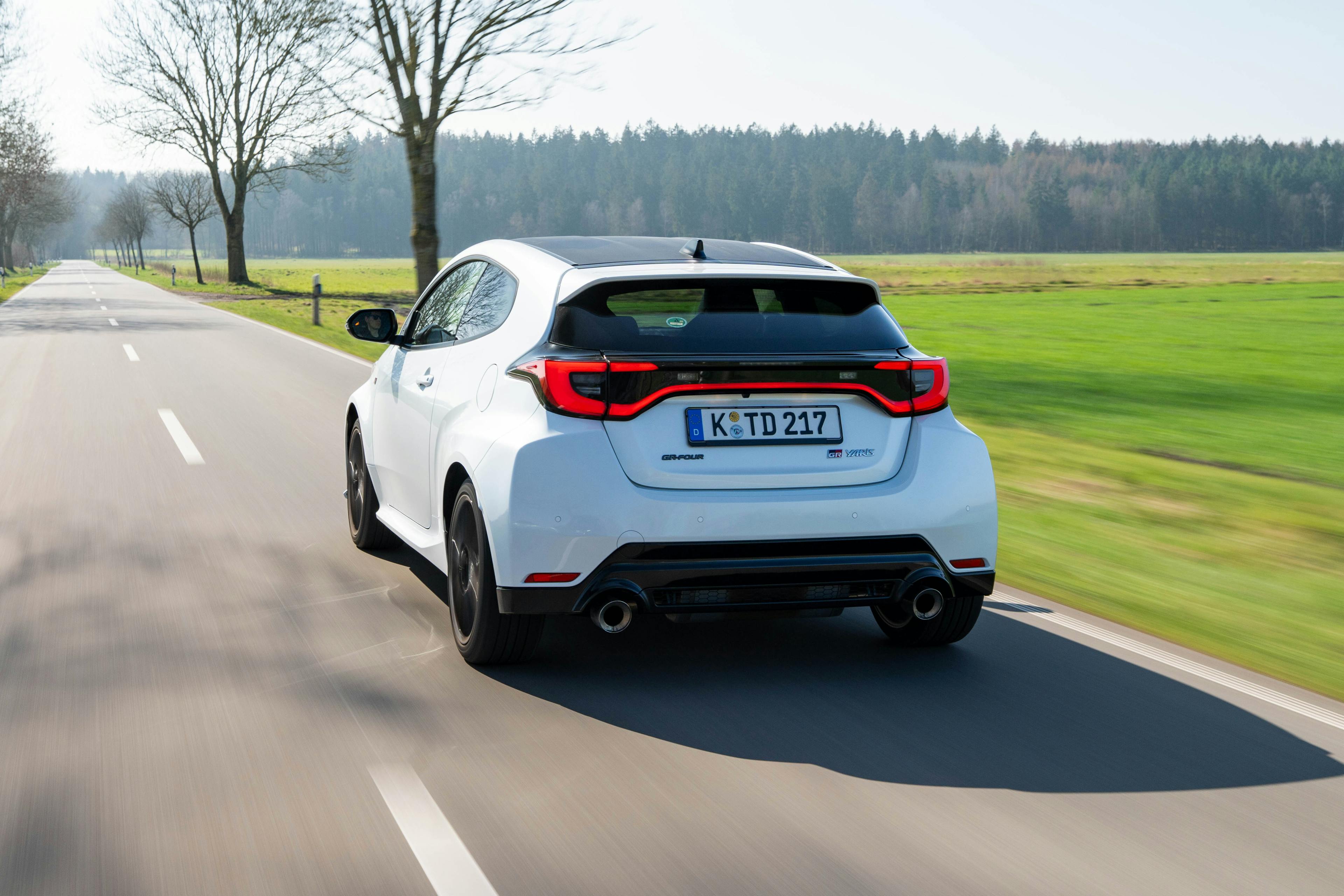 Ein weißer Toyota GR Yaris stehend auf einem Kiesplatz vor grüner Vegetation.
