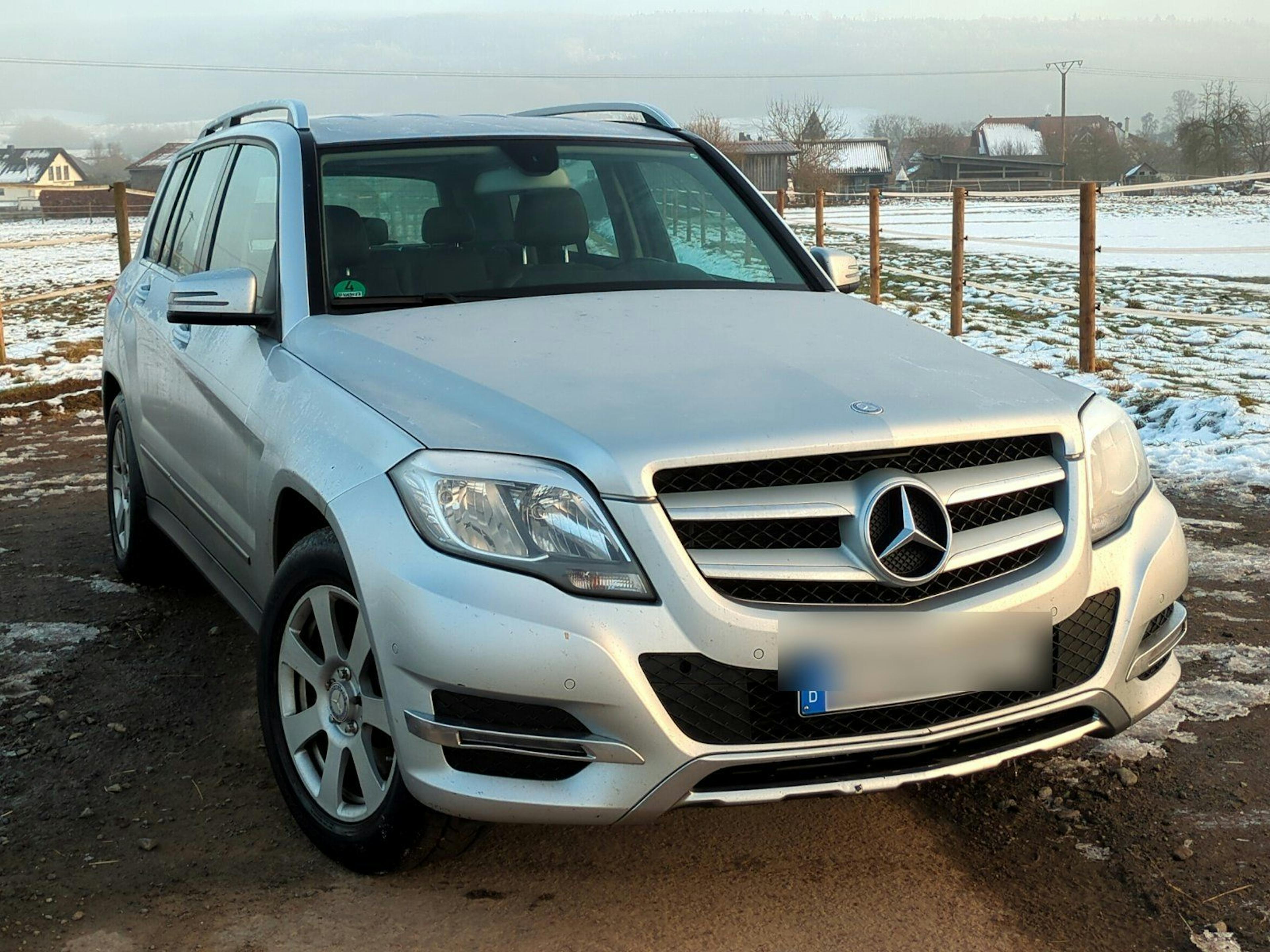 Ein silberner Mercedes-Benz GLK steht auf einem unbefestigten Weg mit schneebedeckter Landschaft im Hintergrund.