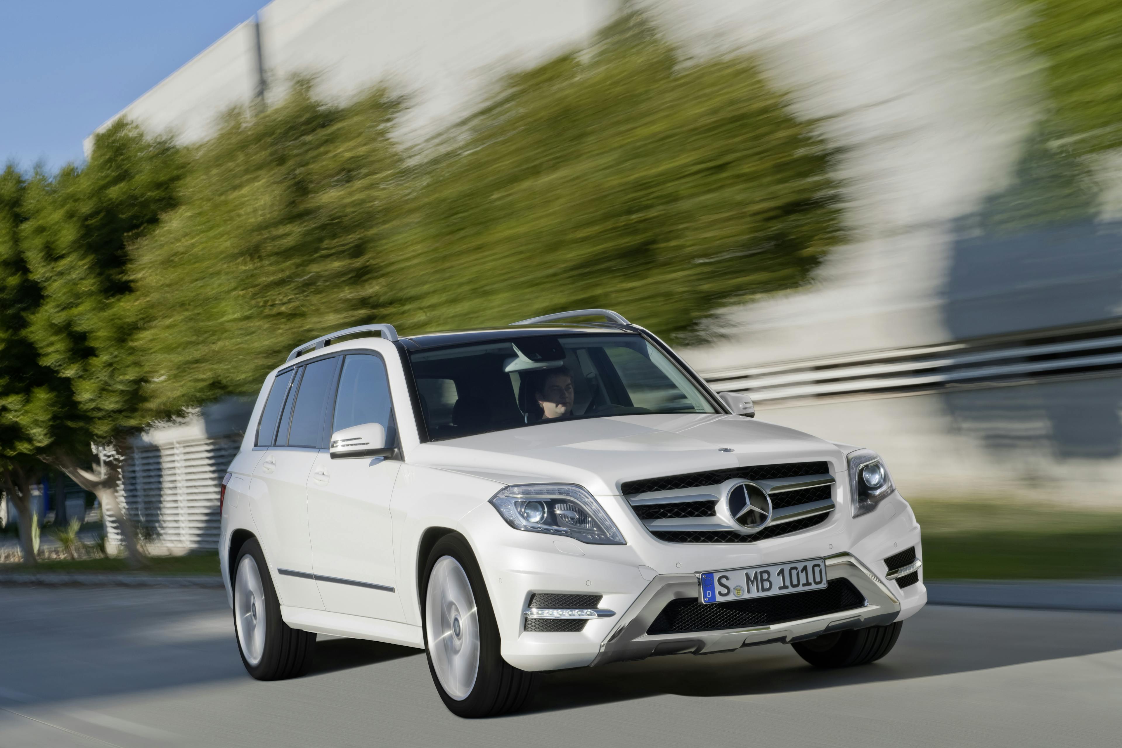 Ein weißer Mercedes GLK fährt vor einer betongrauen Halle entlang.