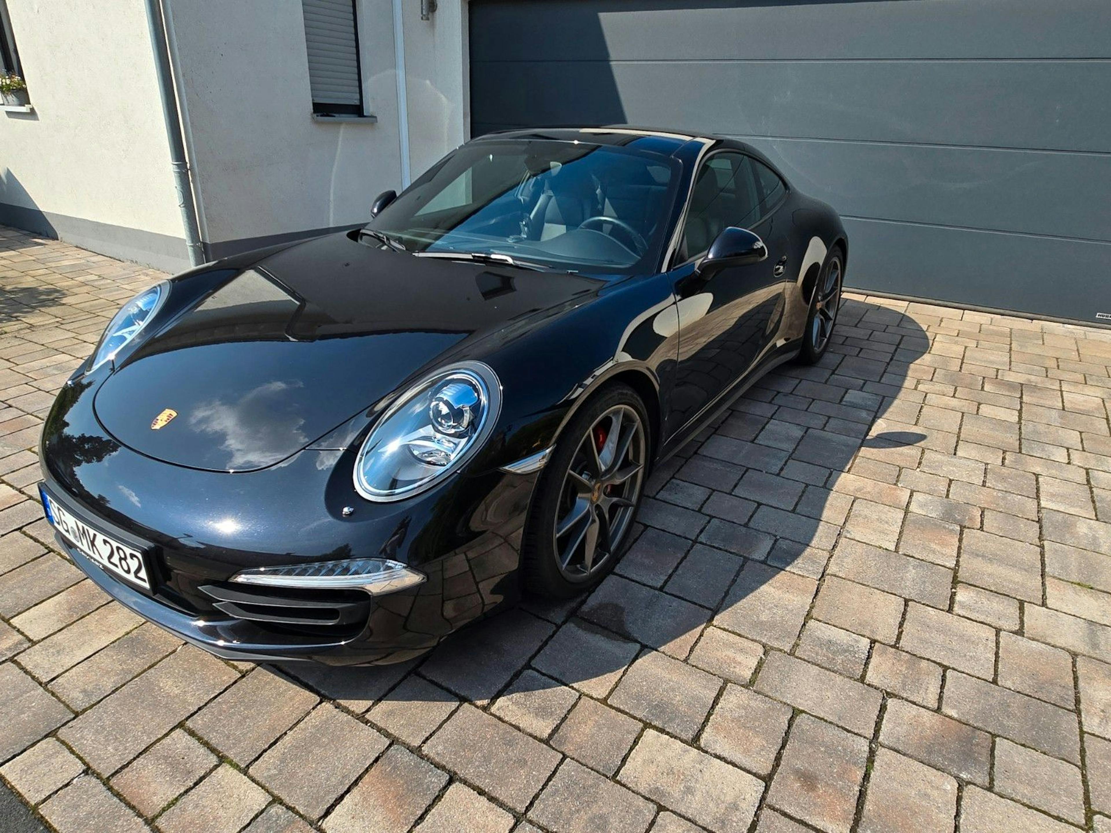Ein schwarzer Porsche 911 Cabrio steht vor einer Garage.